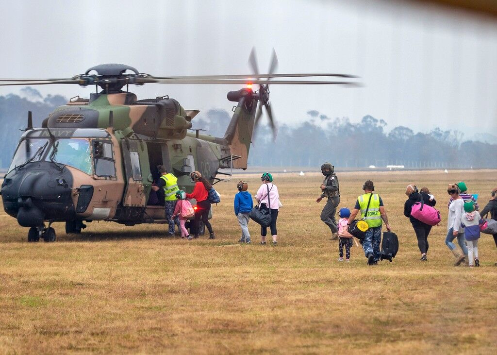 In this photo provided by the Australian Department of Defense, people walk to board a helicopter as the fire ravaged community of Mallacoota is evacuated, Sunday. AP