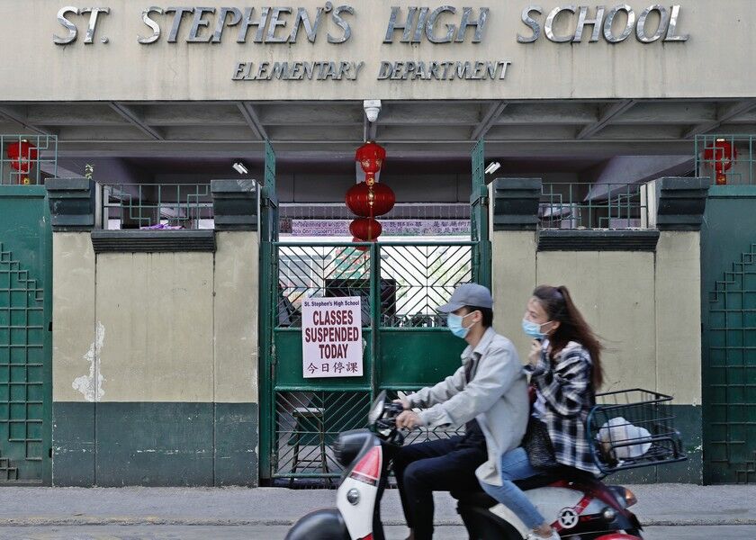 People wearing protective face masks pass by a Chinese-Filipino school that suspended classes in Manila, the Philippines on Monday. AP
