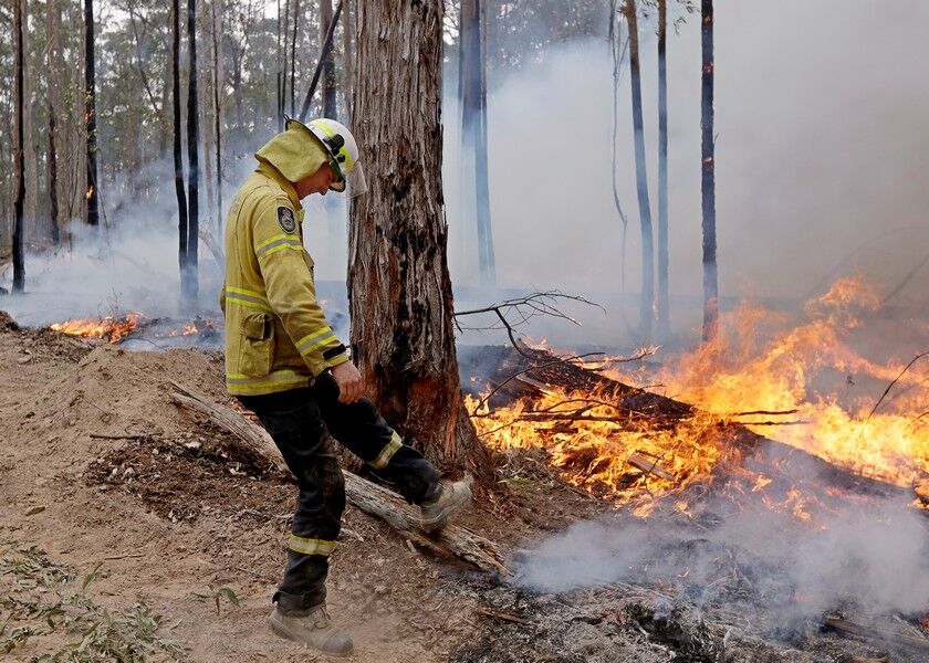 A firefighter kicks at a log while helping to build a containment line at a fire near Bodalla, Australia, Sunday. Authorities are using relatively benign conditions forecast in southeast Australia for a week or more to consolidate containment lines around scores of fires that are likely to burn for weeks without heavy rainfall. AP