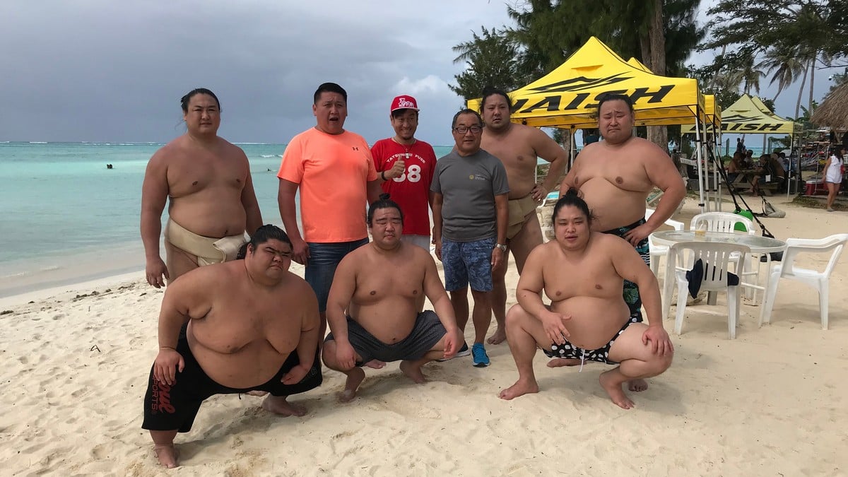 At the Hyatt beach, from left, standing: Kyokutaisei Takuya, Kyokutenho Masaru, Tatsunori Fuse, Hyatt Regency Saipan general manager Nick Nishikawa, Kyokushiuho Koki and Asahisho Kota. Front row, from left: Kaiho Tatsuaki, Kainoryu Hiroki and Kainishiki Tatsuya. Photo by Prince Factor