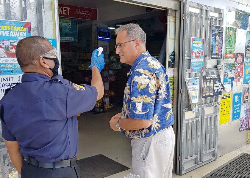 Mamun Mamun of South Pacific Security Services scans the body temperature of a customer at the entrance of Ming Yang Supermarket in San Vicenter. Customers are also provided gloves for shopping. Photos by Bryan Manabat