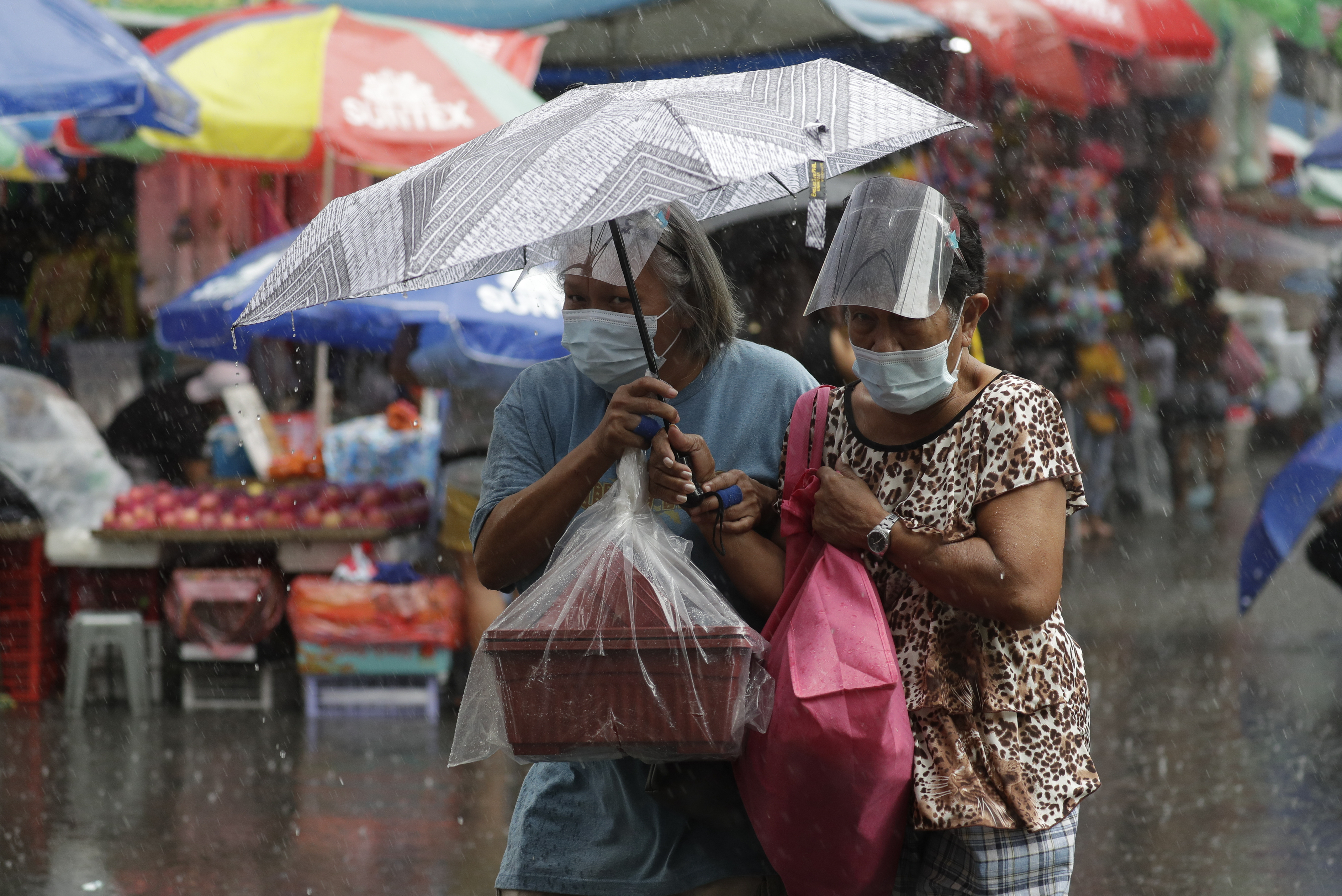Women wearing face masks shelter using an umbrella, in the shopping district of Divisoria in Manila on Dec. 18, 2020. AP