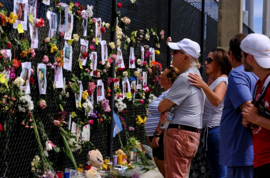People mourn at the memorial site created by neighbors in front of the partially collapsed building where the rescue personnel continue their search for victims, in Surfside near Miami Beach, Florida,  June 26, 2021. 