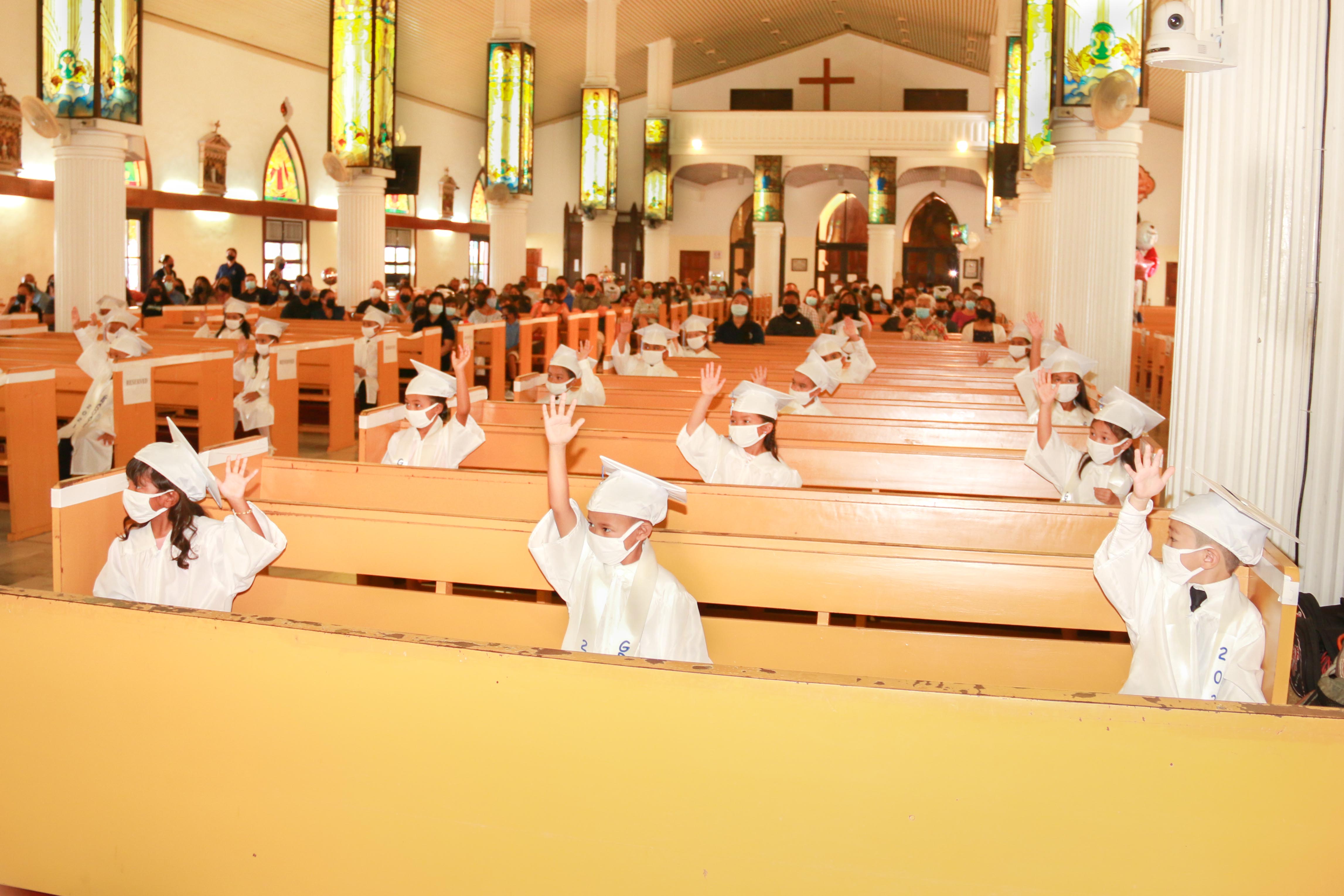Mount Carmel School’s kindergarten promotees  raise their hands during outgoing MCS president Dr. Galvin Deleon Guerrero’s closing remarks at Mount Carmel Cathedral.