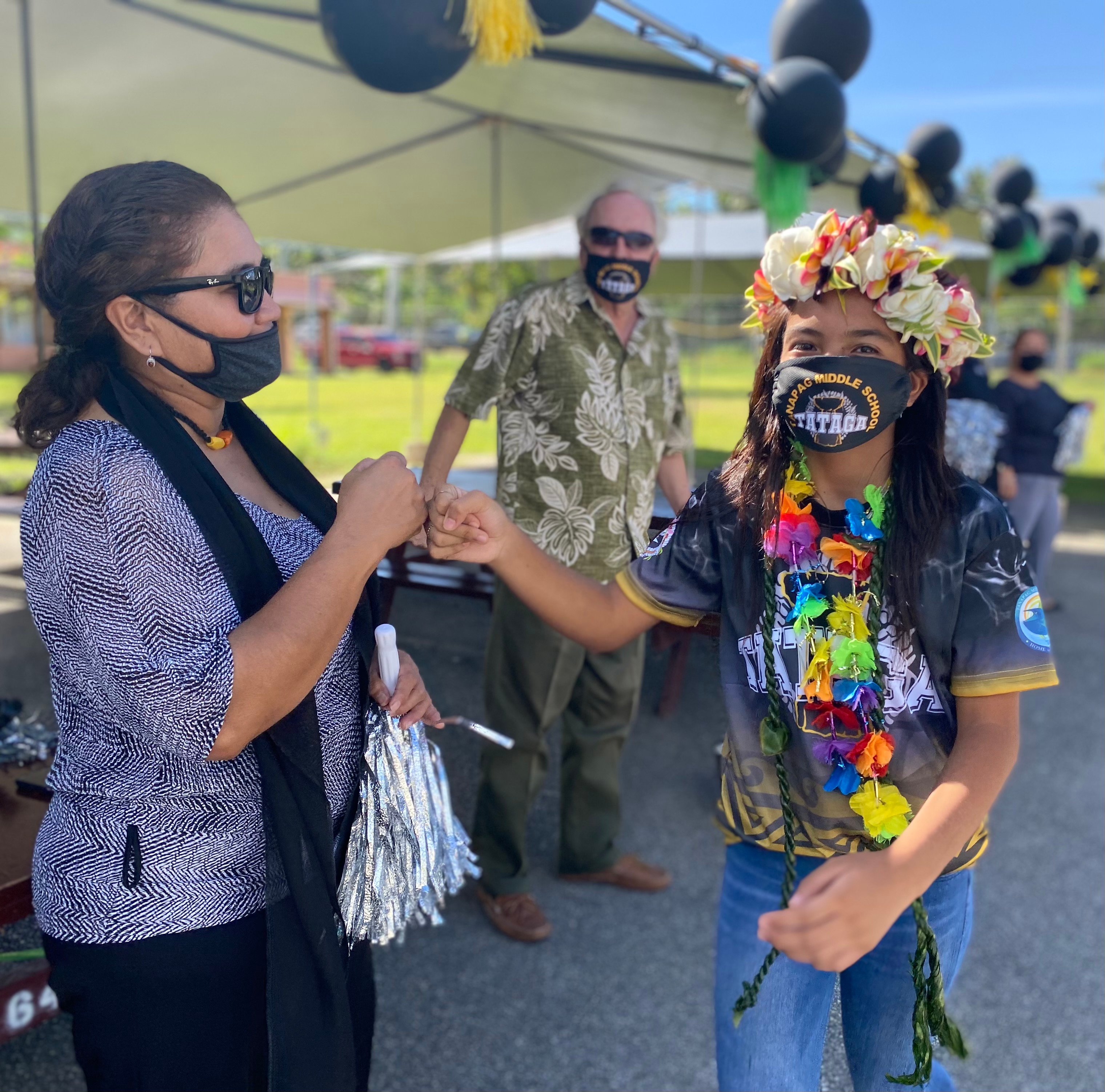 Chacha Oceanview Middle School principal Martha Kintol fist bumps a promoted eighth grader of Tanapag Middle School while Public School System Federal Programs Officer Tim Thornburgh looks on.