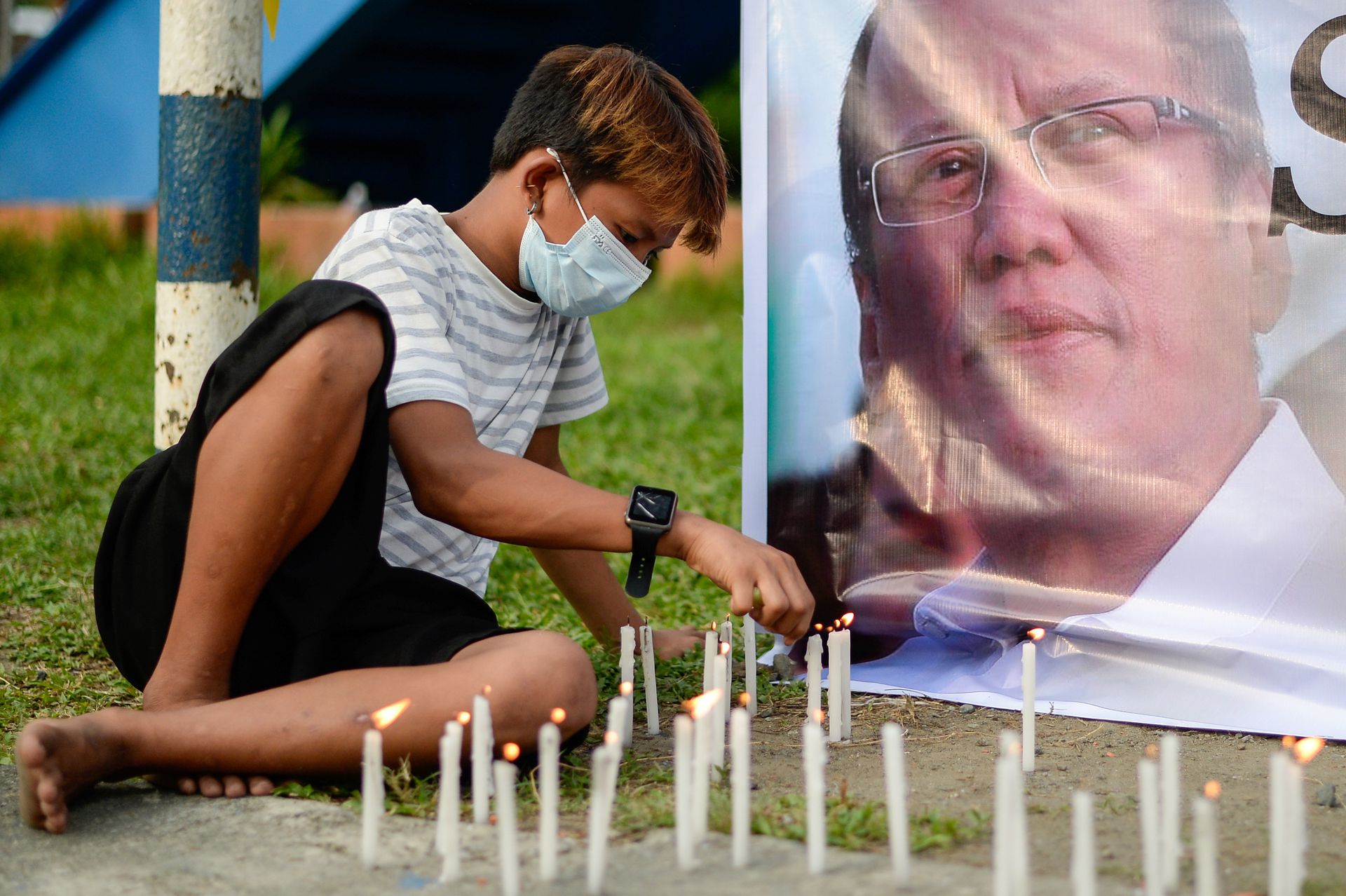 A youth lights a candle beside a tarpaulin of late former Philippine President Benigno Aquino III, outside the Ateneo de Manila University, in Quezon City, Metro Manila, June 25, 2021. 
