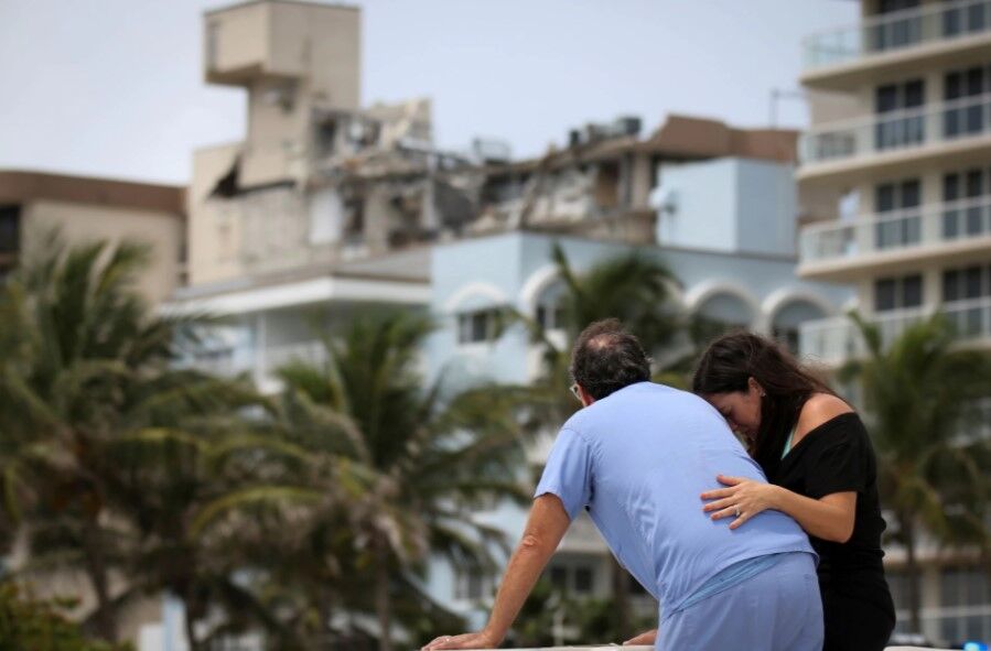 A couple at the beach reacts near the partially collapsed residential building as the emergency crews continue search and rescue operations for survivors, in Surfside, near Miami Beach, Florida,  June 26, 2021. 