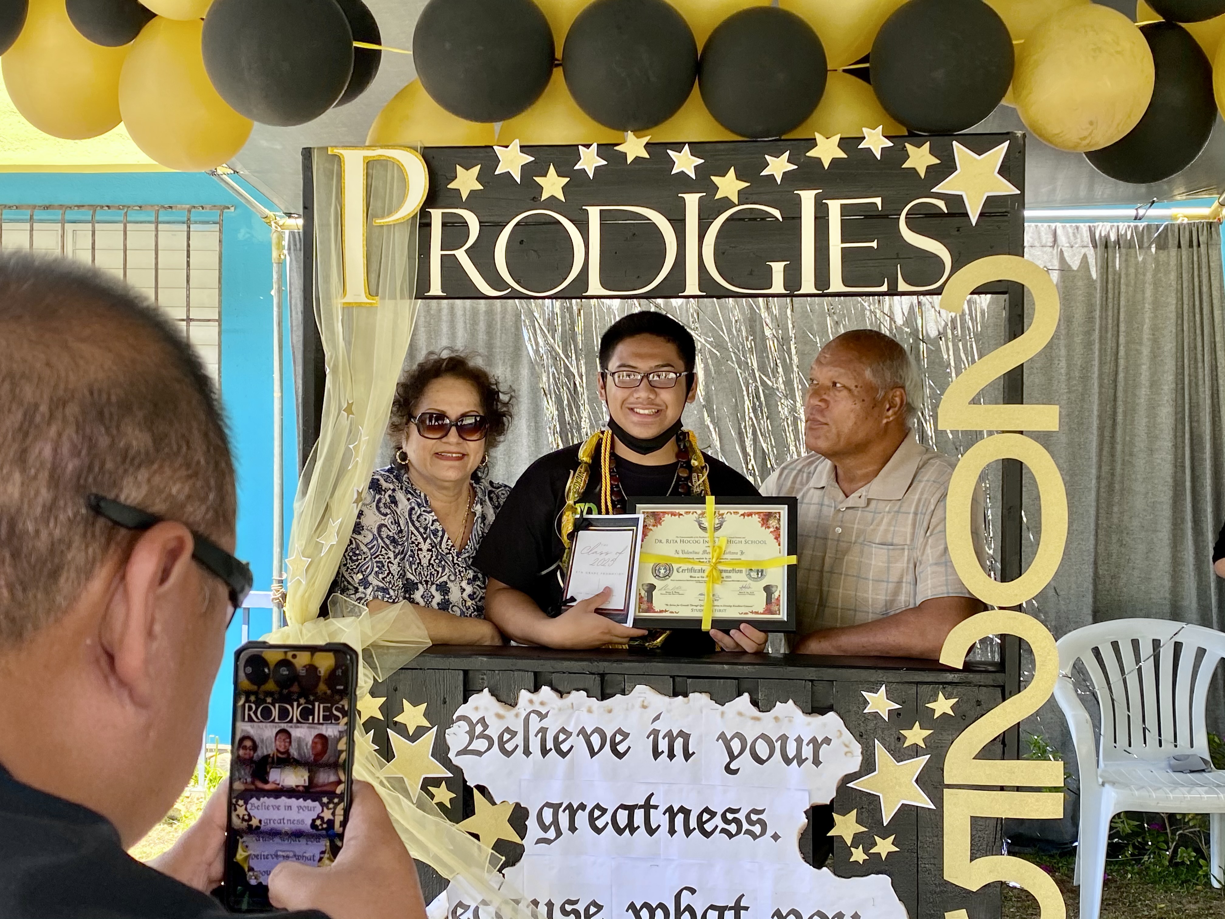 A newly promoted eighth grader poses for a photo with his family.