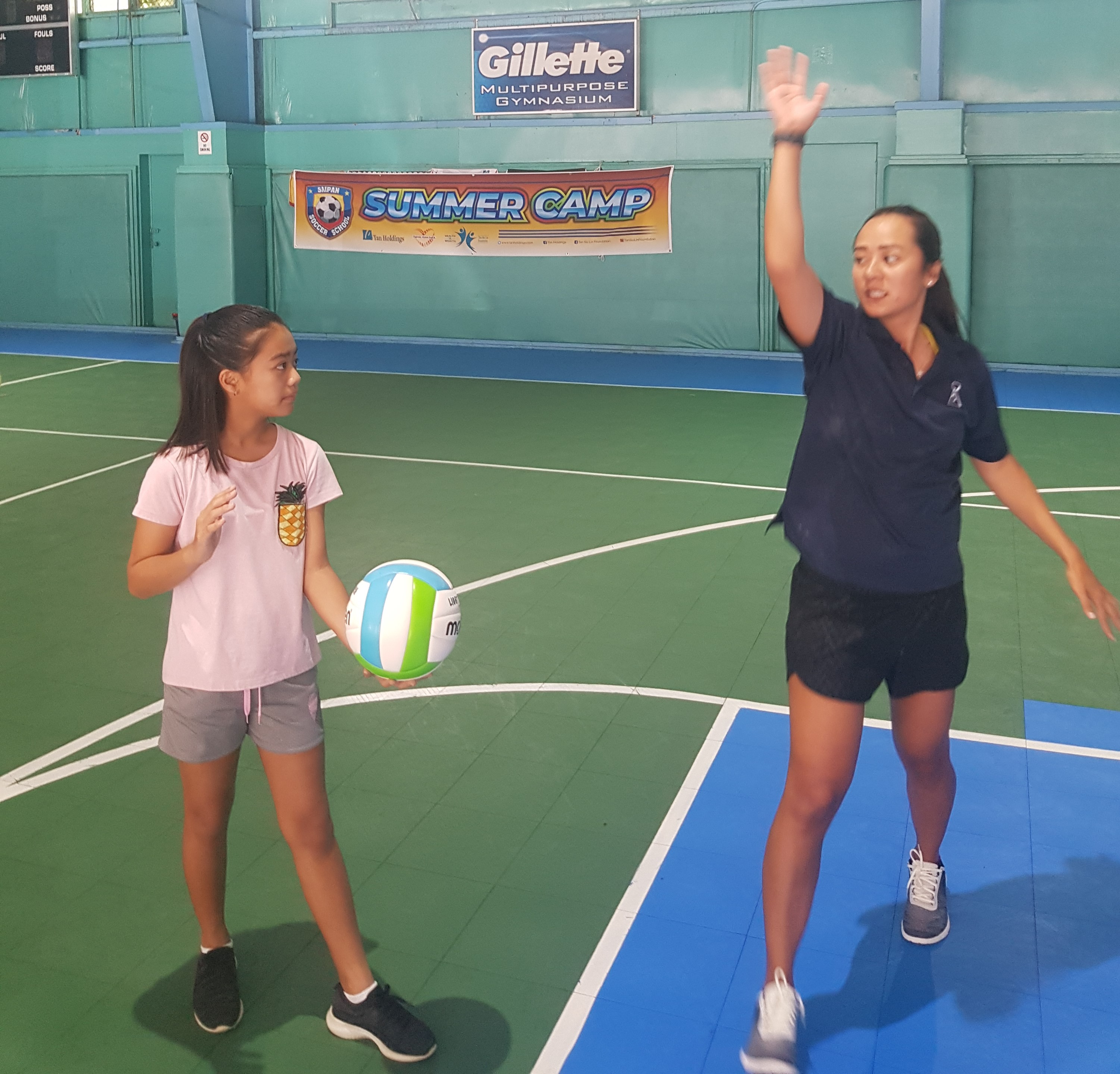 Northern Mariana Islands Volleyball Association president Somia Quan, right, demonstrates to a camp participant the proper way of doing the overhand serve.