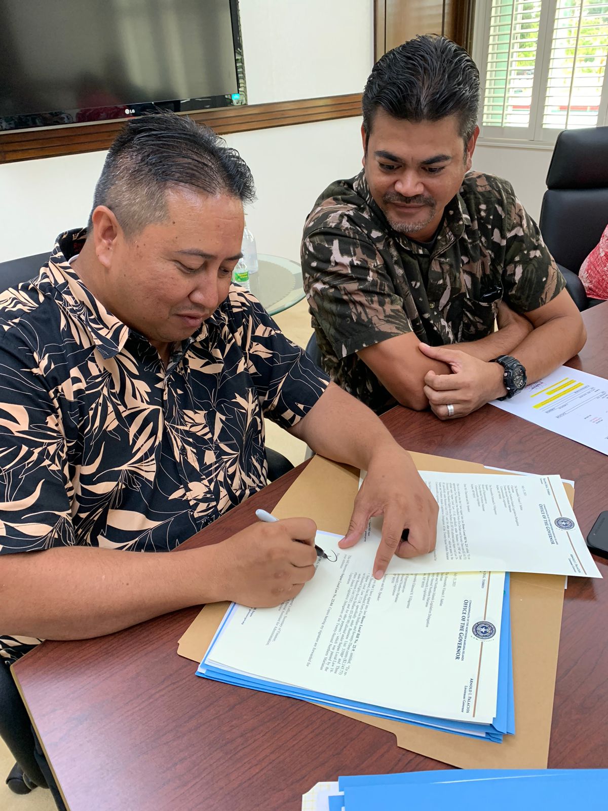 Gov. Ralph DLG Torres signs a bill into law while Rep. Roy A. Ada looks on.
