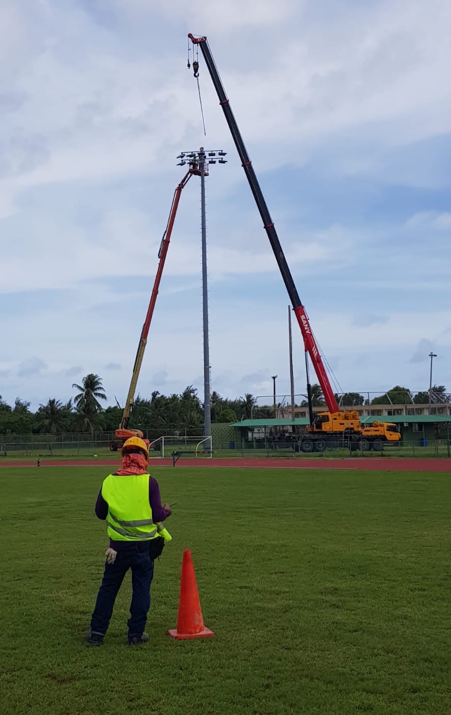 Workers install the lighting fixtures on the metal pole located southeast of the Oleai track and field facility early this month.