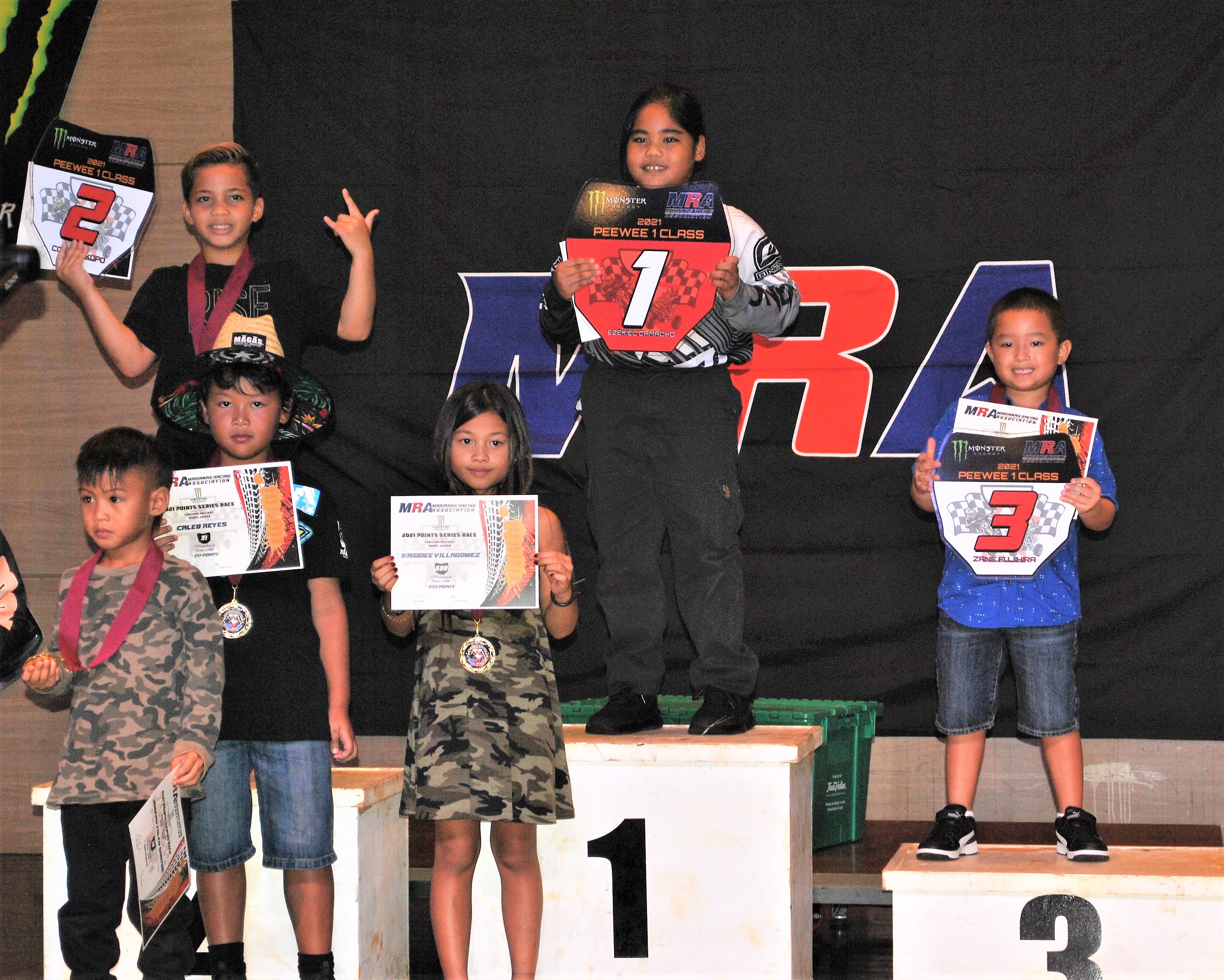 Ezekiel Camacho, center, smiles as he holds the Red Plate trophy of the PeeWee 1 Class next to Conan Iakopo, left, and Zane Fujihira and a few other young riders during the awards banquet of the Marianas Racing Association on July 28 at Saipan World Resort.