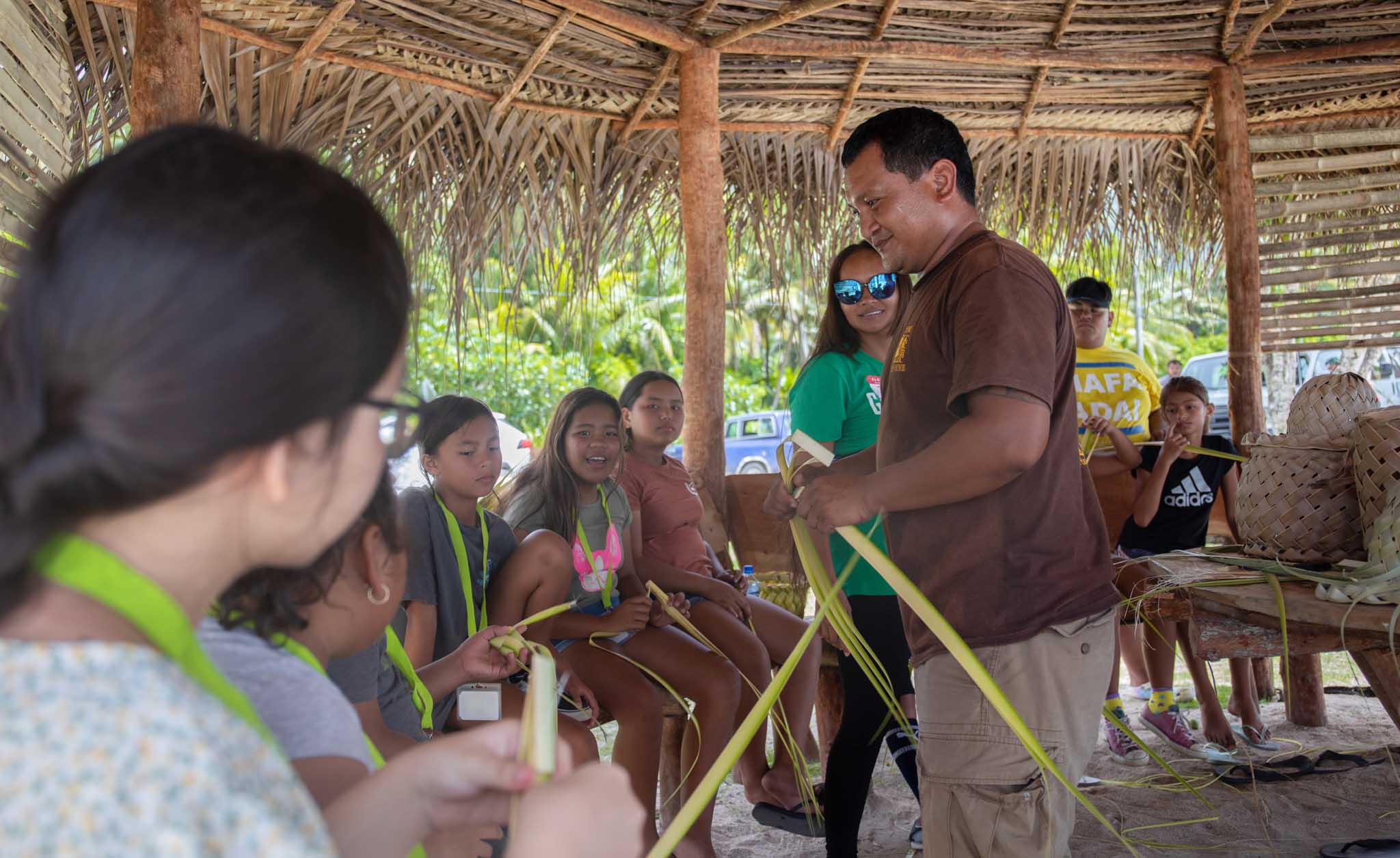 A Department of Community and Cultural Affairs staff member teaches Rota campers and counselors how to weave basic accessories.
