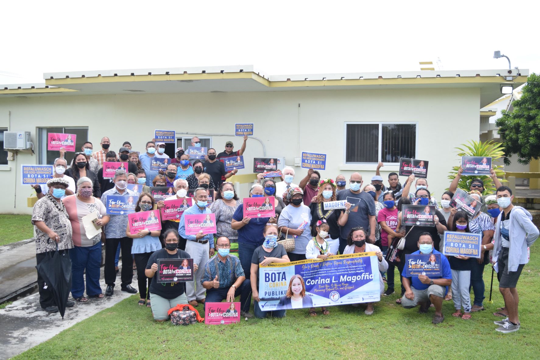 Corina Magofna, her family members, fellow Democrats and other supporters hold signs as they pose for a photo at the Commonwealth Election Commission on Friday.