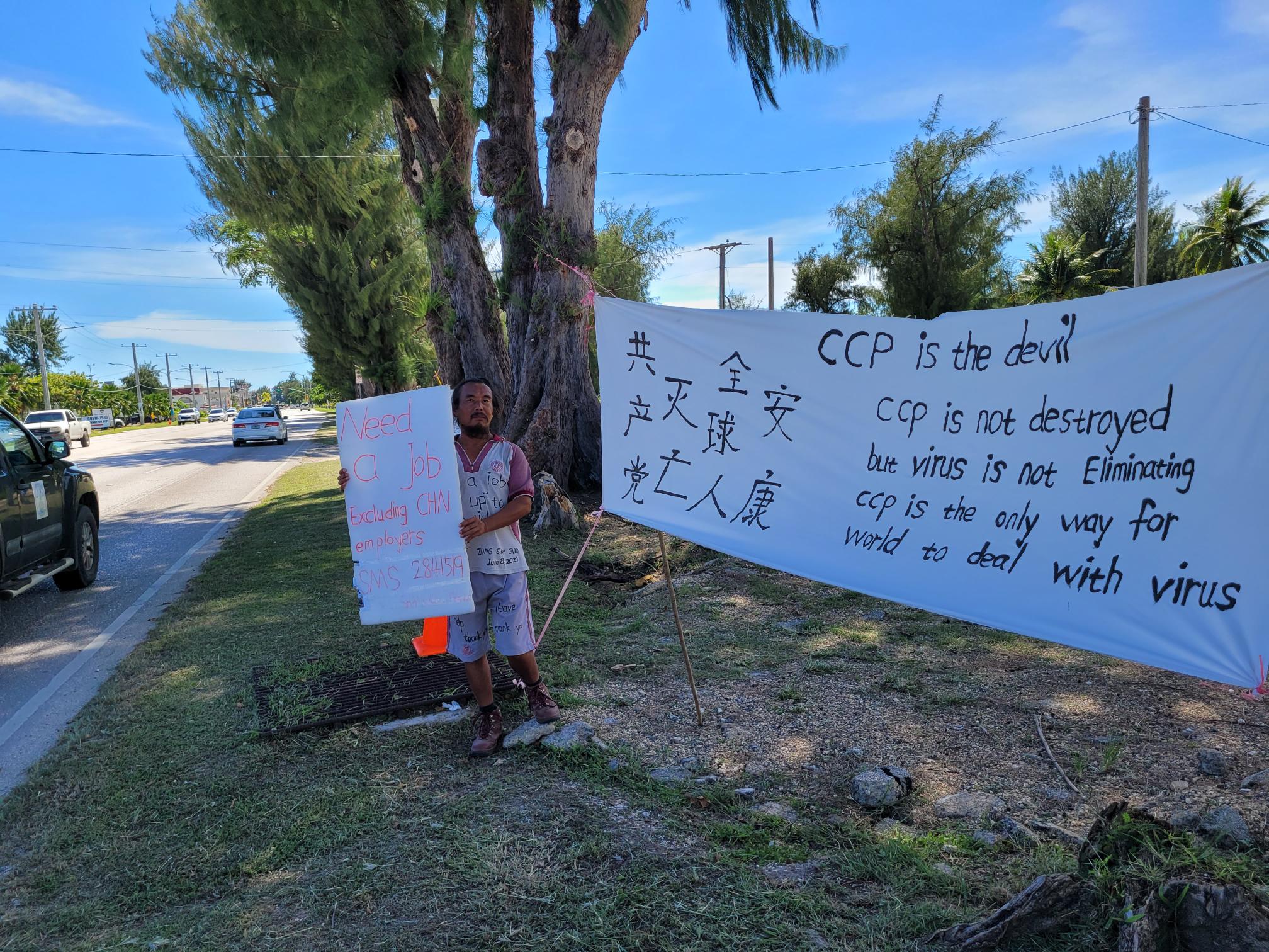 Shanguo Zhang holds a sign during a protest action on Beach Road across from the judicial building in Susupe.