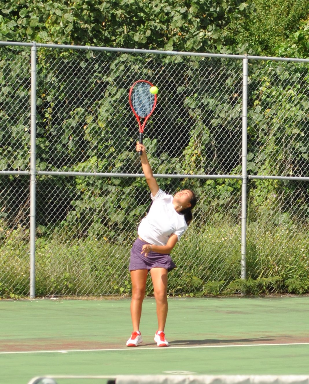 Serin Chung connects an overhand serve during a match at the American Memorial Park tennis court.