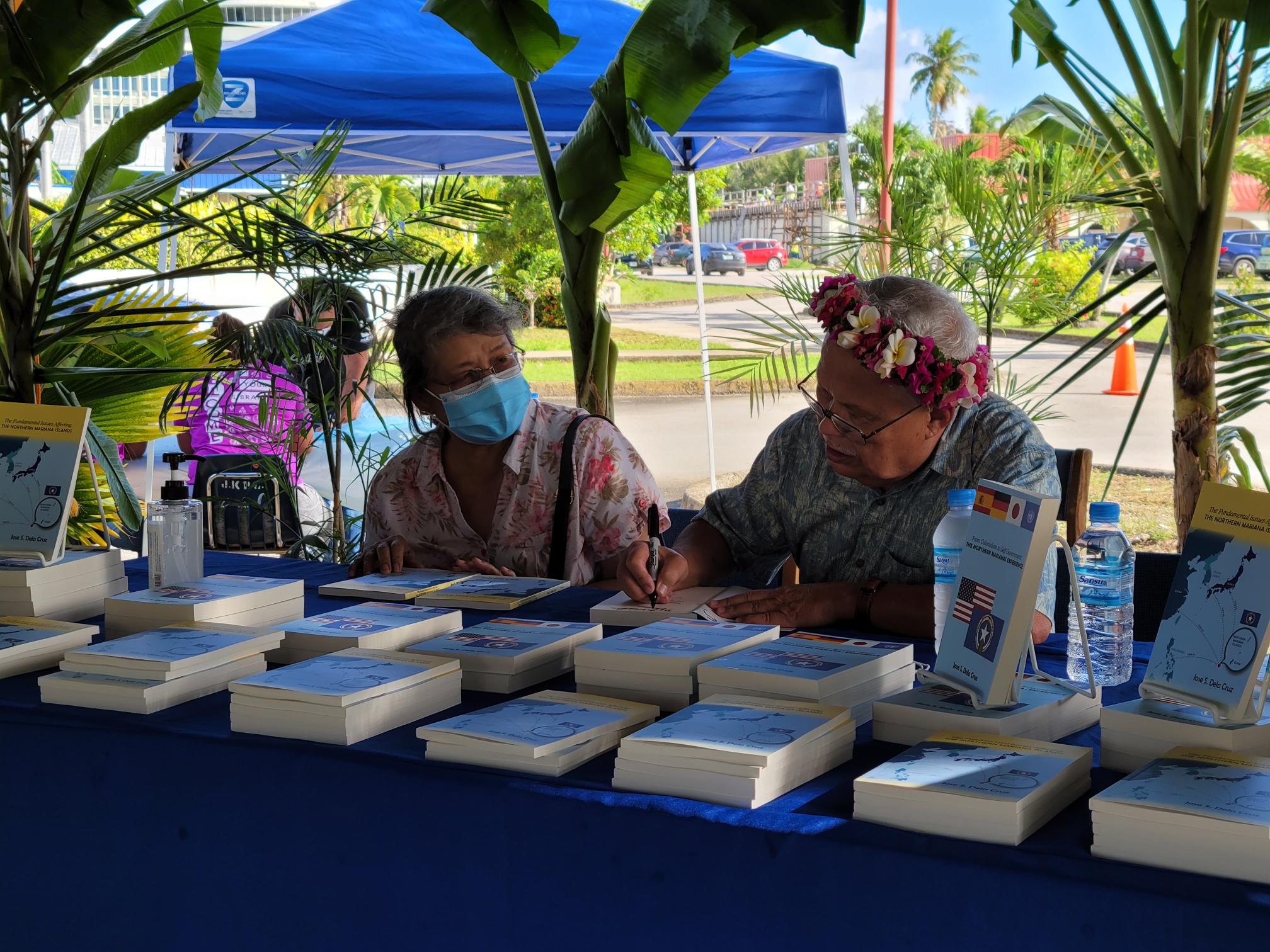 Former CNMI Chief Justice Jose S. Dela Cruz signs a copy of his newest book for former Education Commissioner Dr. Elizabeth Rechebei  Saturday in the Joeten-Kiyu Public Library’s parking lot.