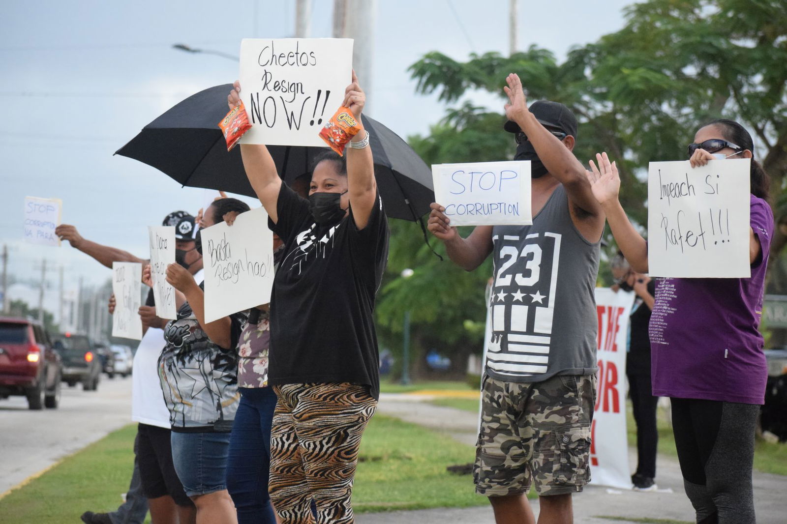 Demonstrators hold signs — and bags of Cheetos — as they call for the impeachment of Gov. Ralph DLG Torres at the Garapan Fishing Base on Tuesday. 