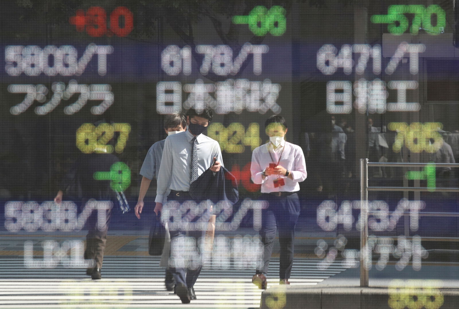 People wearing protective masks are reflected on an electronic board displaying Japan's stock prices outside a brokerage in Tokyo, Oct. 5, 2021.