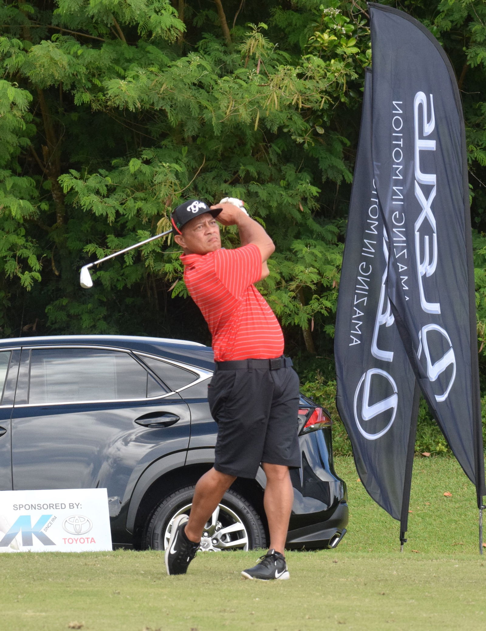 Championship Flight player JJ Atalig swings next to the Hole-in-One prize, Lexus, on Hole No. 13.