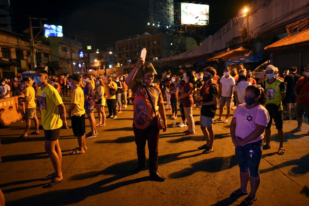 A man sprinkles holy water among Catholic devotees attending a mass on the feast day of the Black Nazarene, outside Quiapo Church in Manila on Jan. 9, 2021.