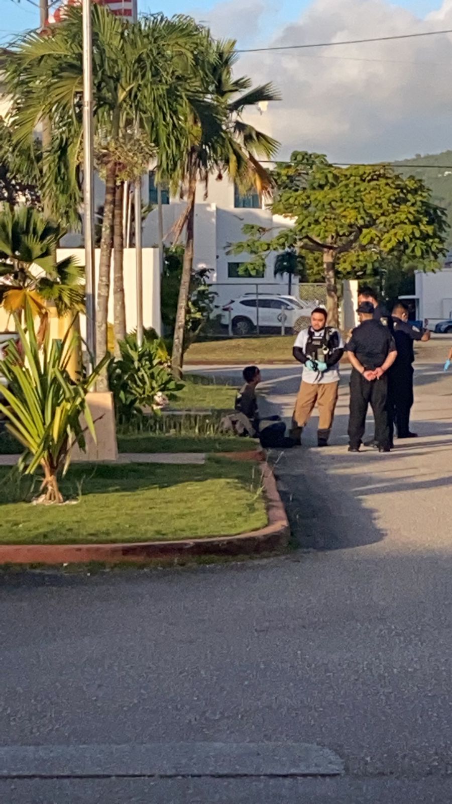 Bradley Hocog in handcuffs is seated on a curb while talking with police officers at the Department of Public Safety headquarters late Monday afternoon.