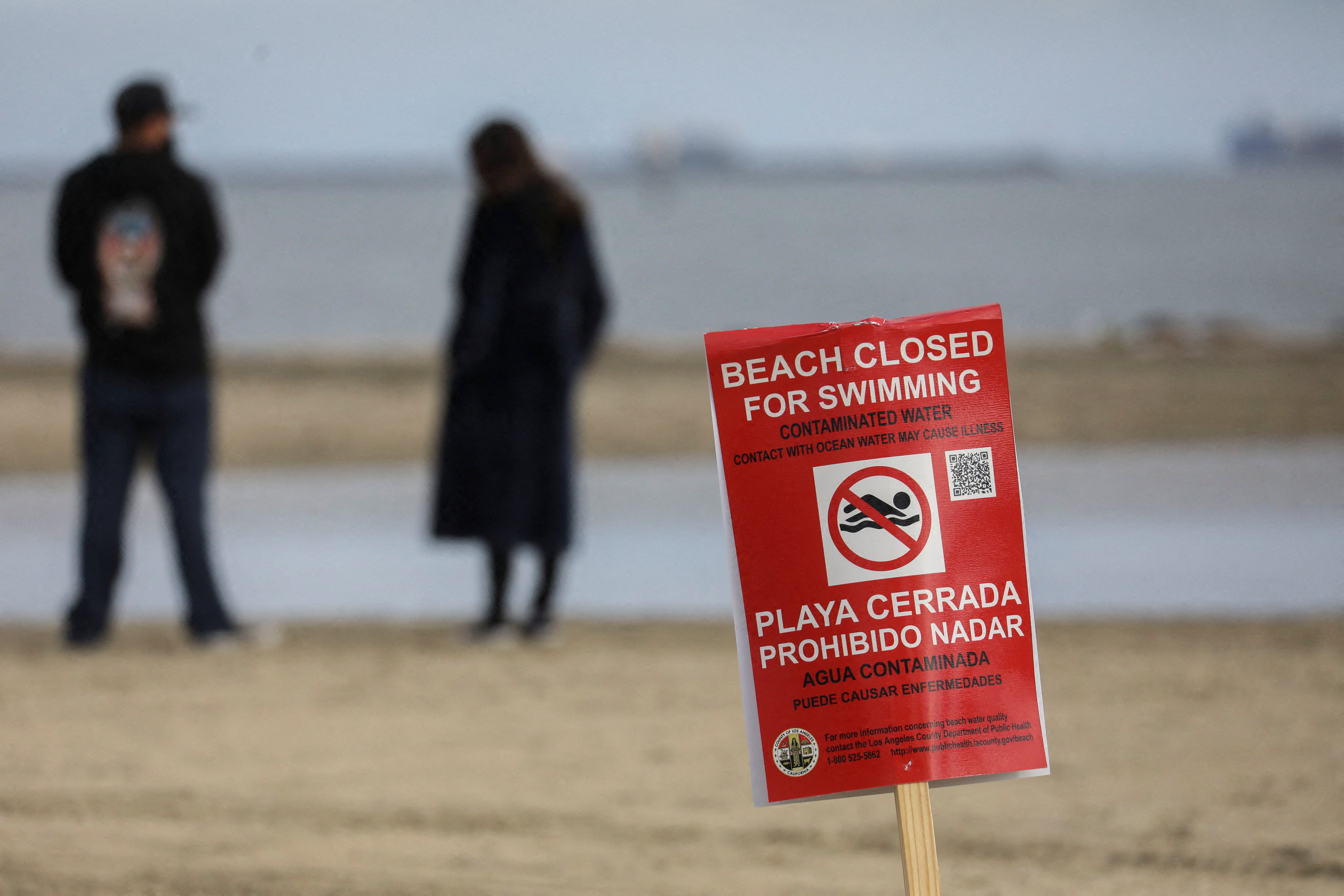 A sign warns swimmers after the city of Long Beach closed the beaches due to a report of a spill of between two and four million gallons of untreated sewage into a canal in Carson, at Cabrillo Beach in Long Beach, California, Dec. 31, 2021.