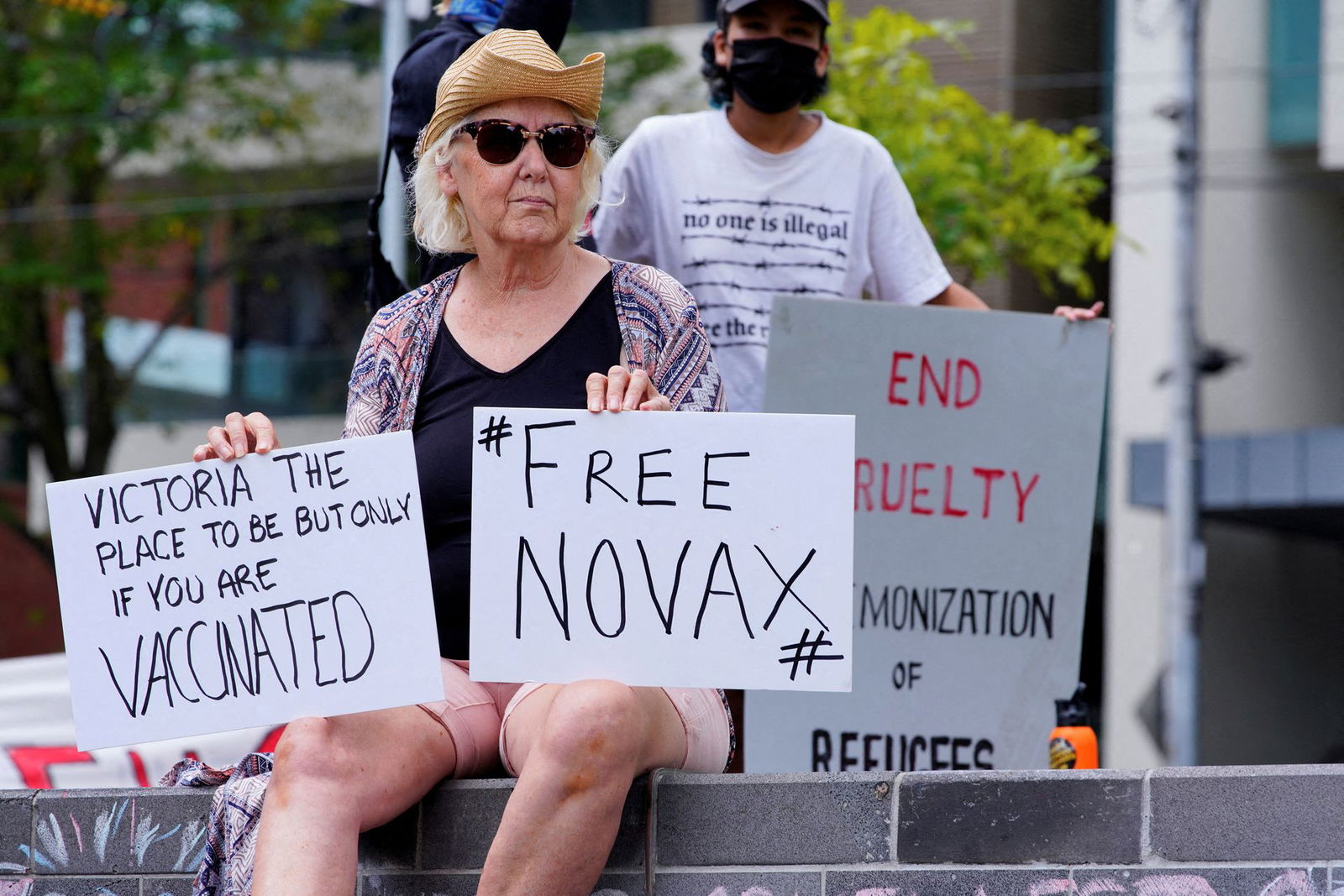 A protestor holds signs outside the Park Hotel, where Serbian tennis player Novak Djokovic is believed to be staying in Melbourne, Australia, Jan. 6, 2022.