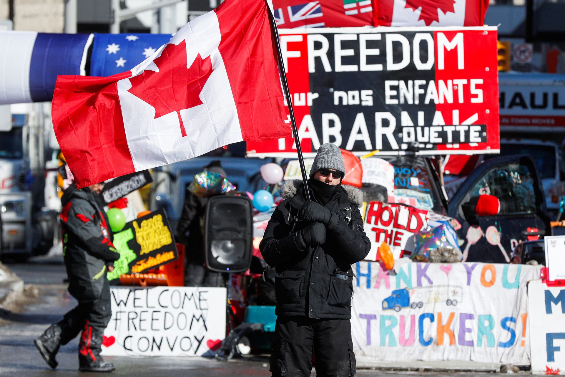 A person waves a Canadian flag in front of banners in support of truckers, as truckers and supporters continue to protest the coronavirus disease vaccine mandates, in Ottawa, Ontario, Canada, Feb. 14, 2022.