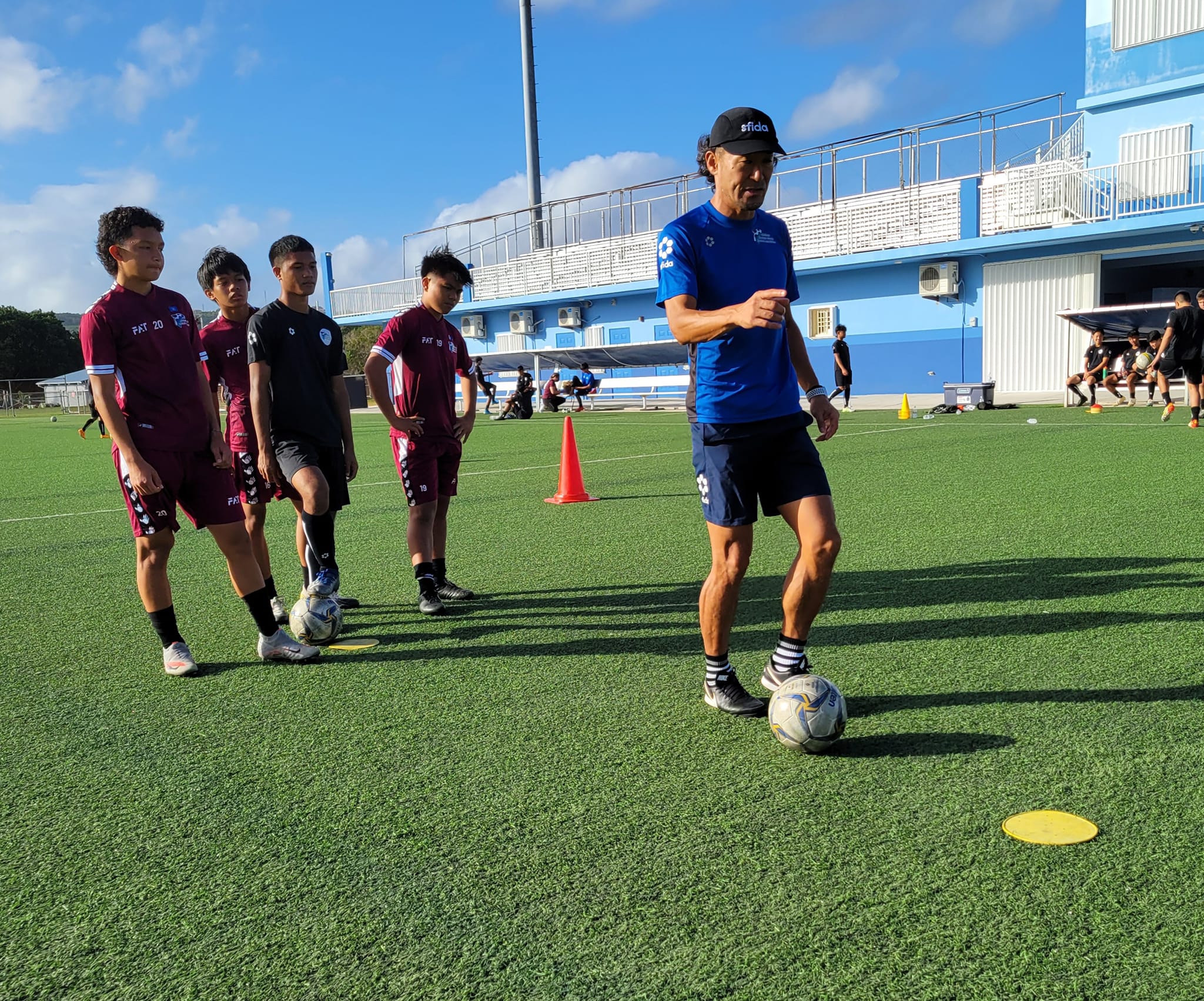 NMI players watch coach Michiteru Mita demonstrates passing and ball control drills in one of their practice sessions last week during the training camp at the Guam Football Association National Training Center.