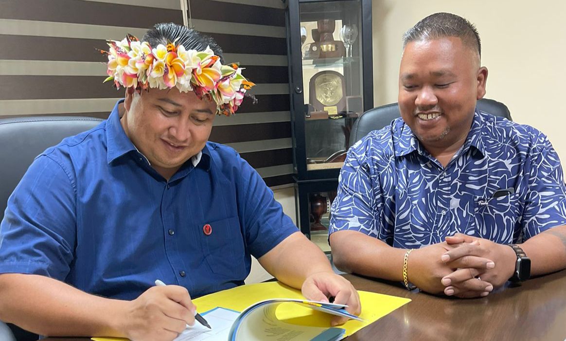 Gov. Ralph DLG Torres signs House Bill 22-81 into law as its author, Rep. Angel Demapan, looks on Friday in the governor's office.