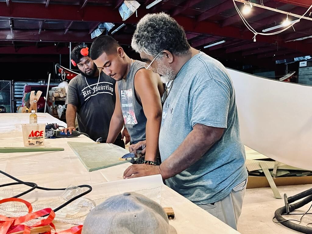 Senior Sakman Leader & Master Navigator Mario Benito, right, assesses the measurements of a small model of a Carolinian canoe with some members of his team: boatbuilders Lolobeyong Benito, center, and Timothy Onopey, left.