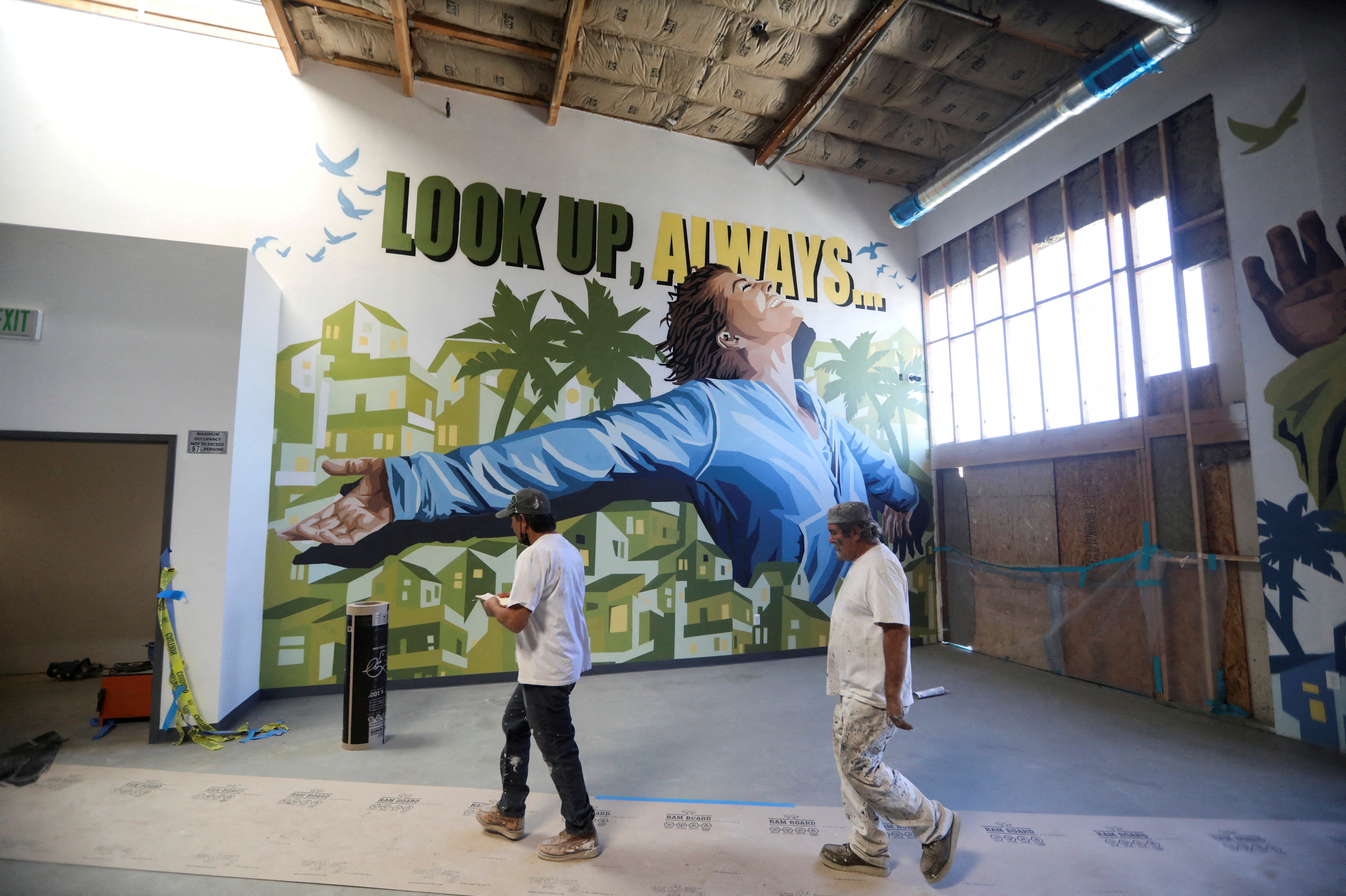 Construction workers pass in front of a mural at Carnegie Shelter, which is currently under construction in Santa Ana, California, March 2, 2022.