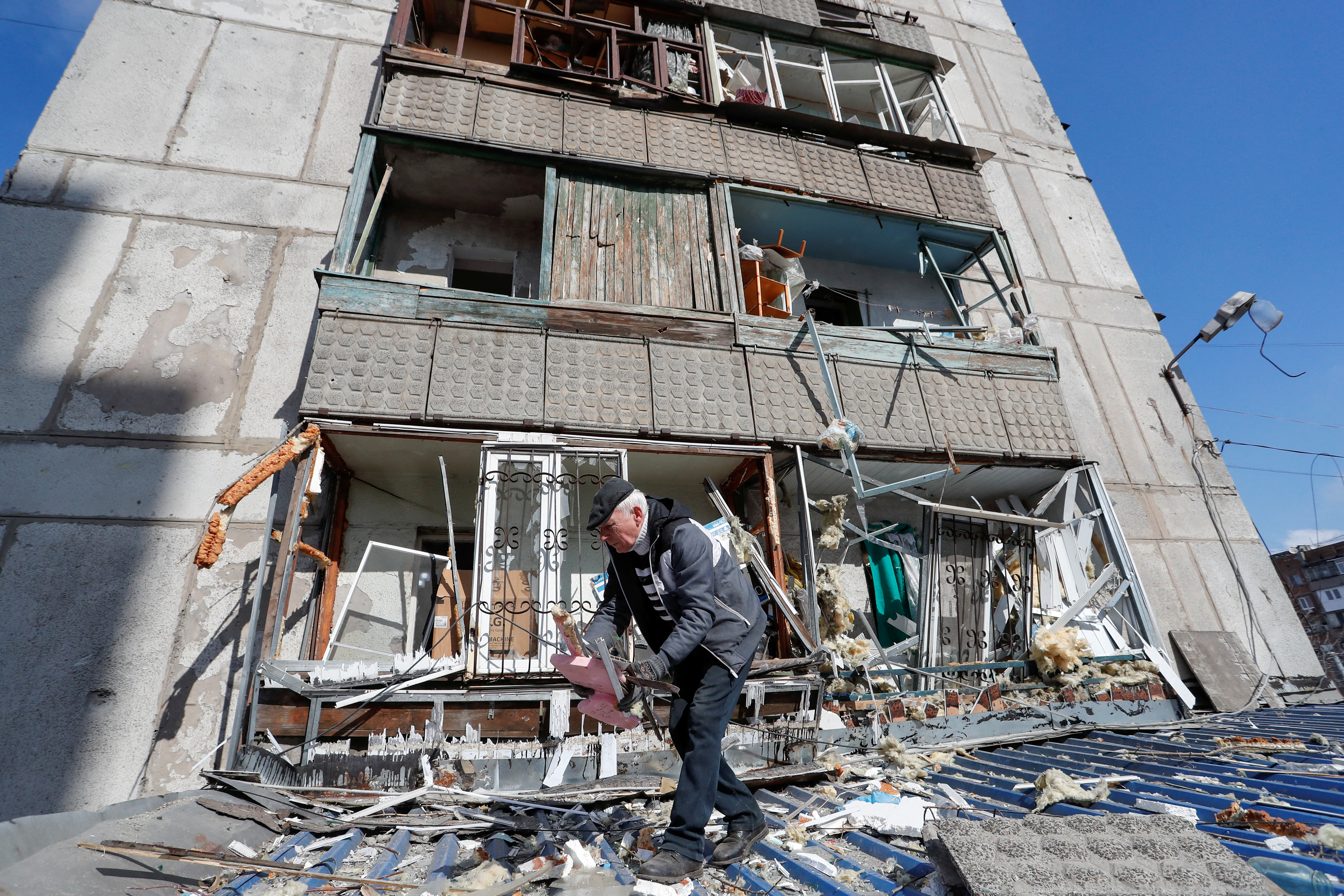 A man removes debris outside a residential building damaged by shelling during Ukraine-Russia conflict in the separatist-controlled town of Makeyevka or Makiivka outside Donetsk, Ukraine, March 16, 2022.