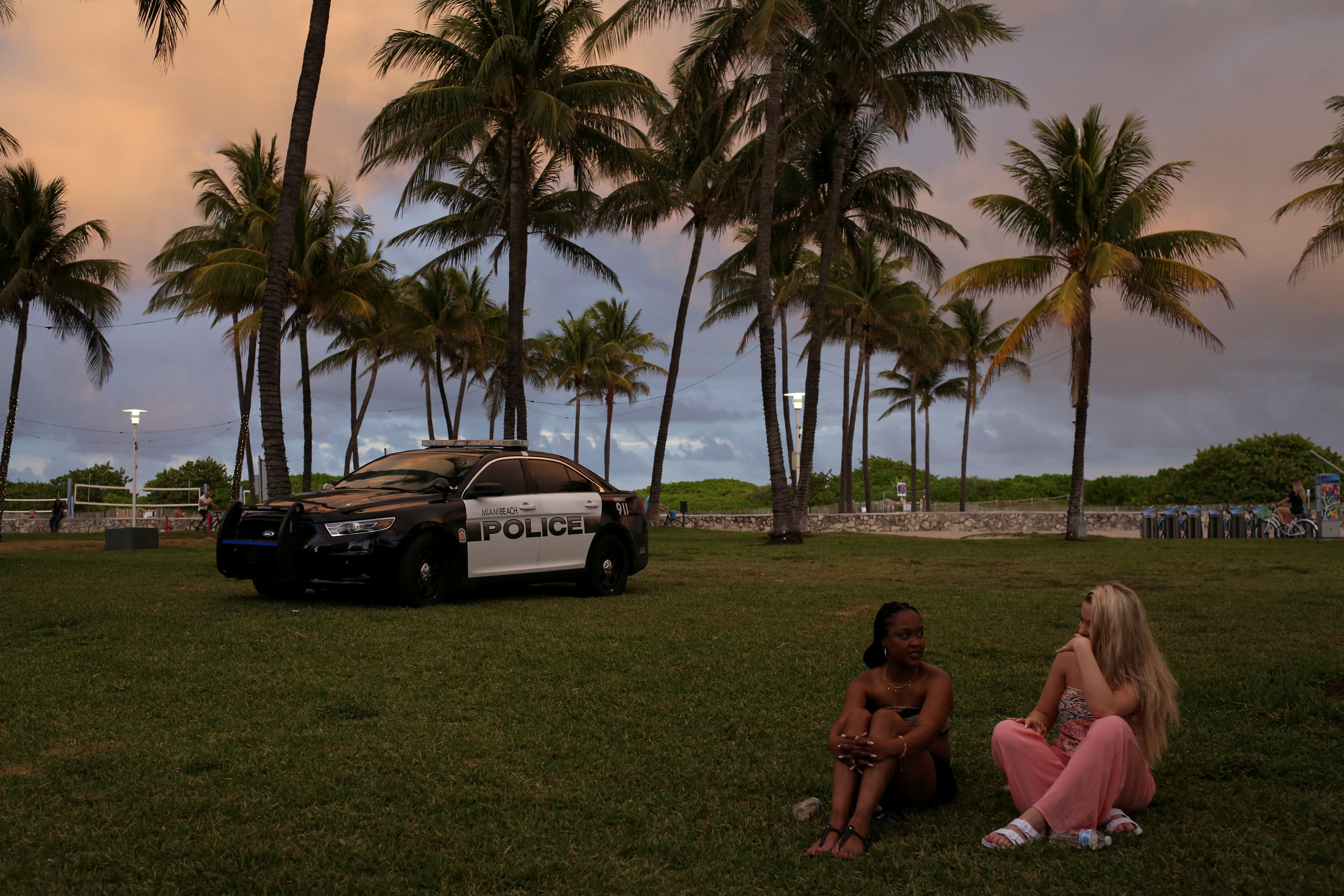 A police vehicle is seen next to people enjoying spring break, ahead of an 8 p.m. curfew imposed by local authorities amid the coronavirus disease pandemic, in Miami Beach, Florida, March 27, 2021.