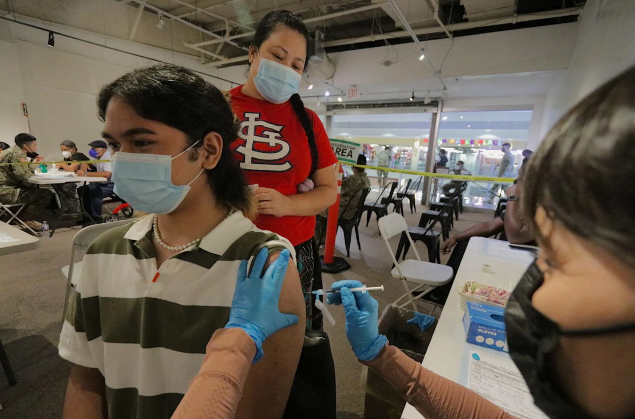 George Washington High School senior Lee Apimwar, 17, left, is accompanied by his mother Marian Sony, center, as he receives his second dose of the Moderna vaccine during the first day of the Covid-19 vaccination clinic at the Agana Shopping Center Monday.