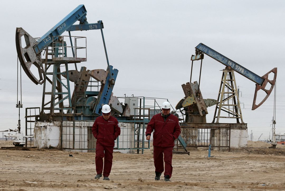 Workers walk as oil pumps are seen in the background in the Uzen oil and gas field in the Mangistau Region of Kazakhstan on Nov. 13, 2021.