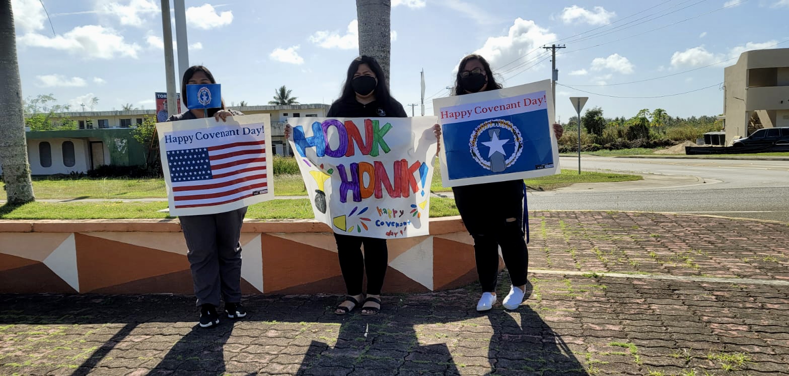 Honk for Covenant Day! Tinian Junior-Senior High School employees carry signs during their roadside waving activity.
