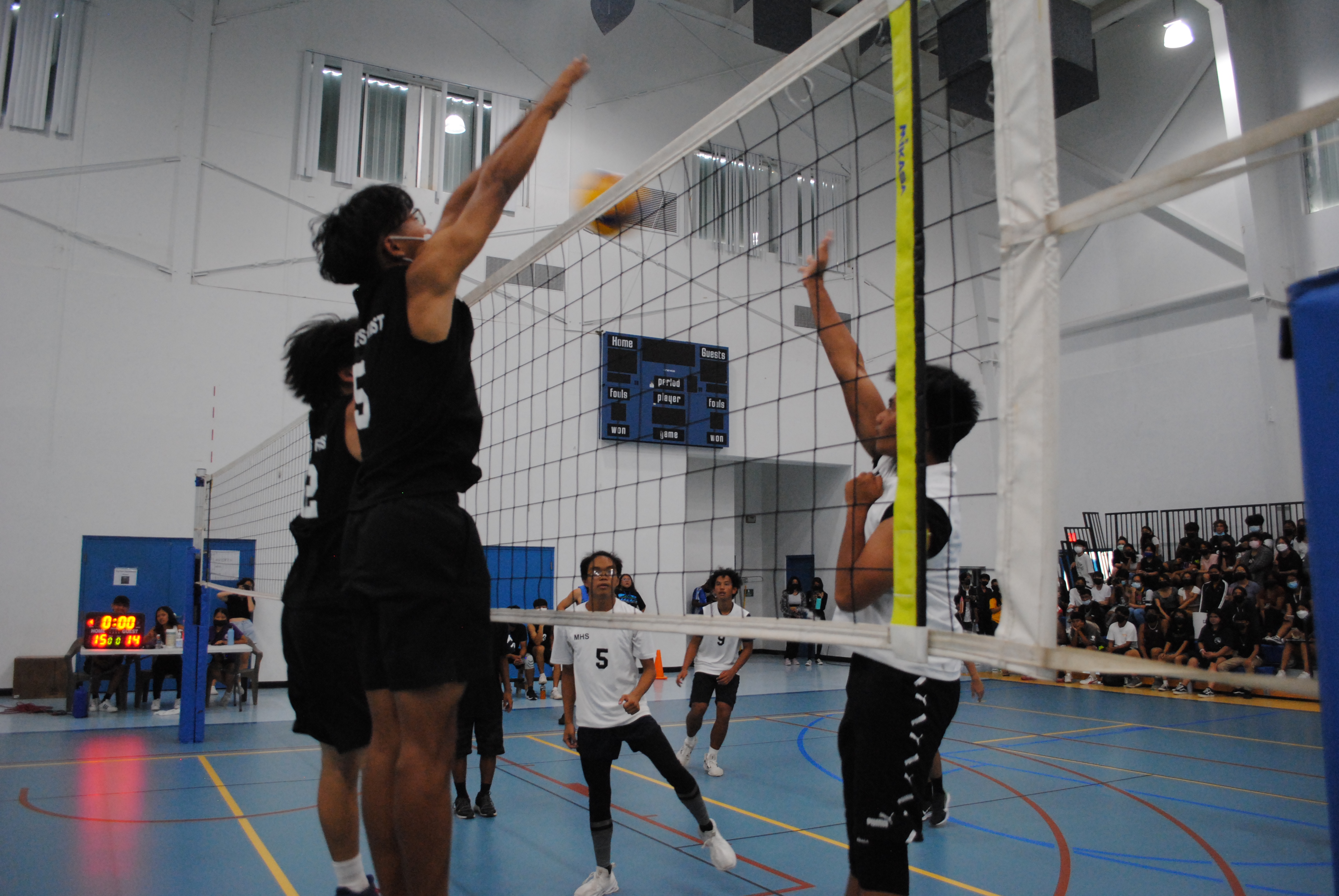 An MHS 2 player tips the ball over as two MHS 3 defenders extend for the block during a PSS Boys High School Volleyball game Saturday at the MHS gym.
