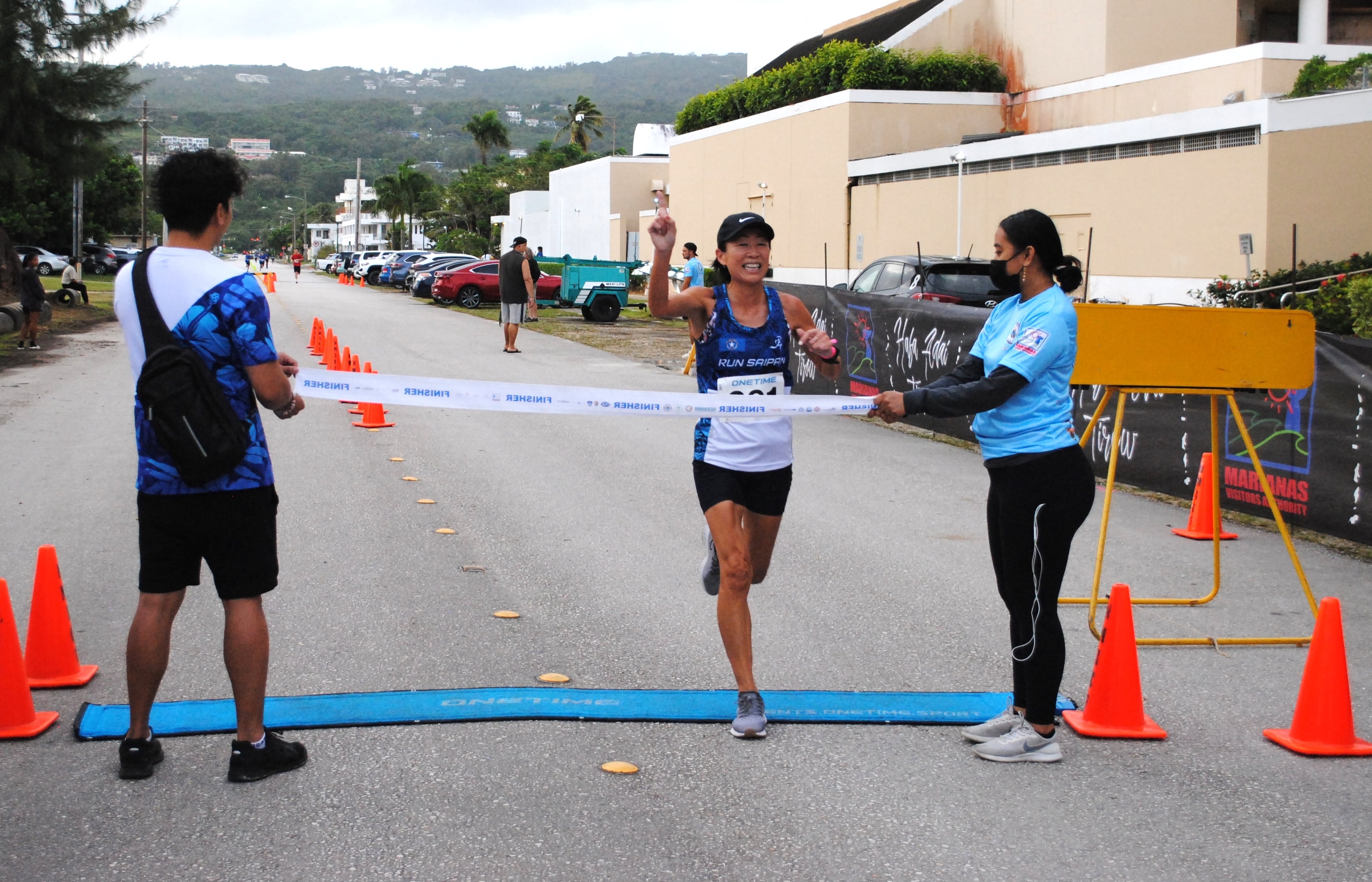 A smiling Noriko Jim gestures as she crosses the finish line of the Saipan Half Marathon/5K race Saturday at  American Memorial Park.