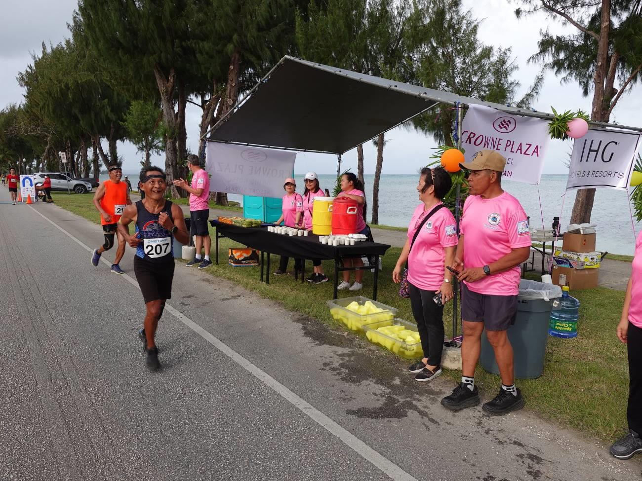 Volunteers at Crowne Plaza Resort Saipan aid station cheer on Carlos Aguilar of Northern Marianas and other participants of Saipan Marianas 2022 on April 9, 2022.