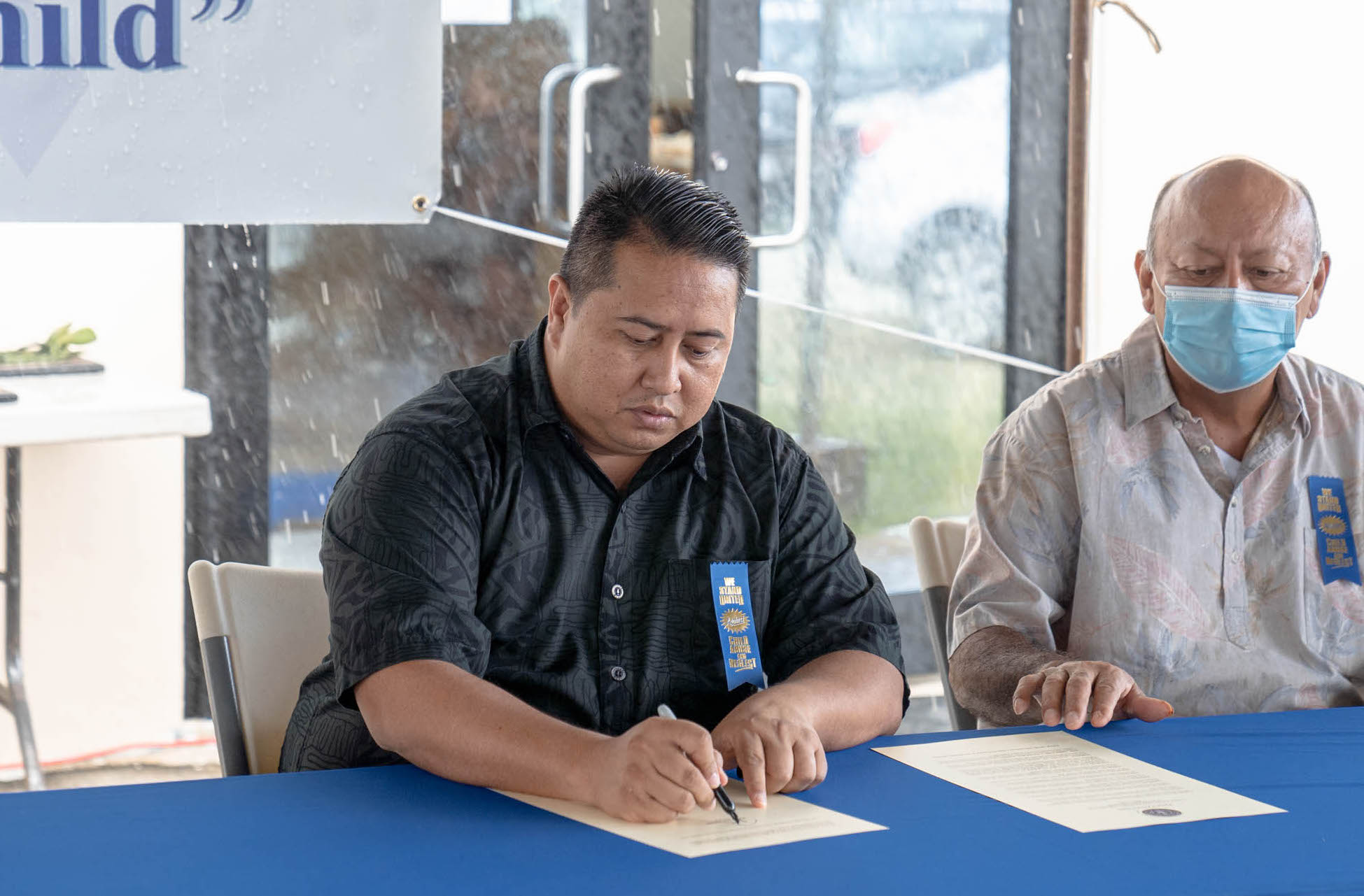 Gov. Ralph DLG Torres signs the Child Abuse and Neglect Prevention and Awareness Month proclamation while Department of Cultural and Community Affairs Secretary Joseph P. Deleon Guerrero looks on.