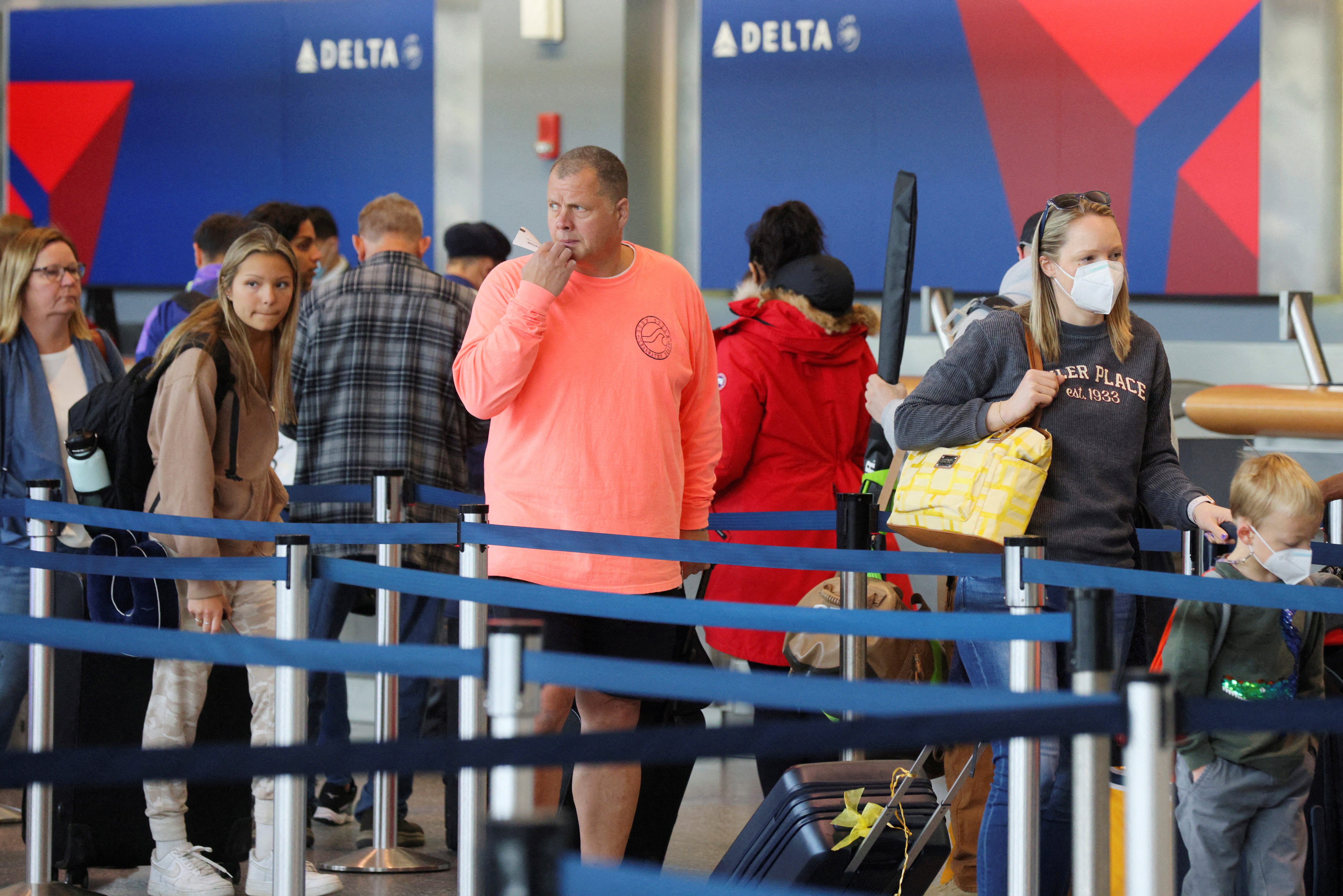 Travelers wearing masks and not wearing masks wait in line at a Delta Airlines counter at Logan International Airport in Boston, Massachusetts, April 19, 2022.
