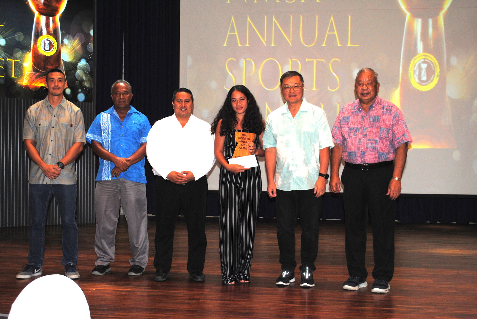 Kina Rangamar, 3rd right, receives the NMI Sports Hall of Fame Award on behalf of Irminia Pua. Also in photo are NMI Sports Hall of Fame committee members James Lee, left, Ray Tebuteb, 2nd left, Gov. Ralph DLG Torres,  3rd left, Northern Marianas Sports Association President Jerry Tan, 2nd right, and Saipan Mayor David Apatang, right, during the NMSA Annual Sports Banquet on Tuesday at the Kensington Hotel Saipan.