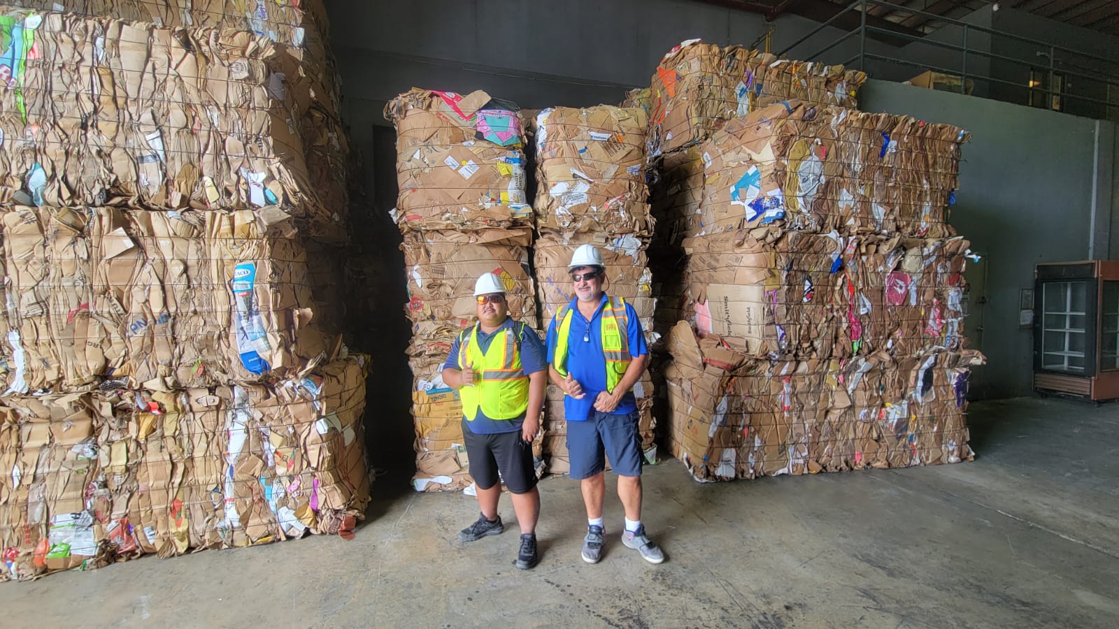 Department of Public Works Tinian Branch Manager of the Solid Waste Division Ray Lazaro and DPW Tinian Resident Department Head Joal Untalan share a photo together at the Mr. Rubbishman Transfer Station in Guam. Behind them are cardboard bales weighing 1.2 tons each.
