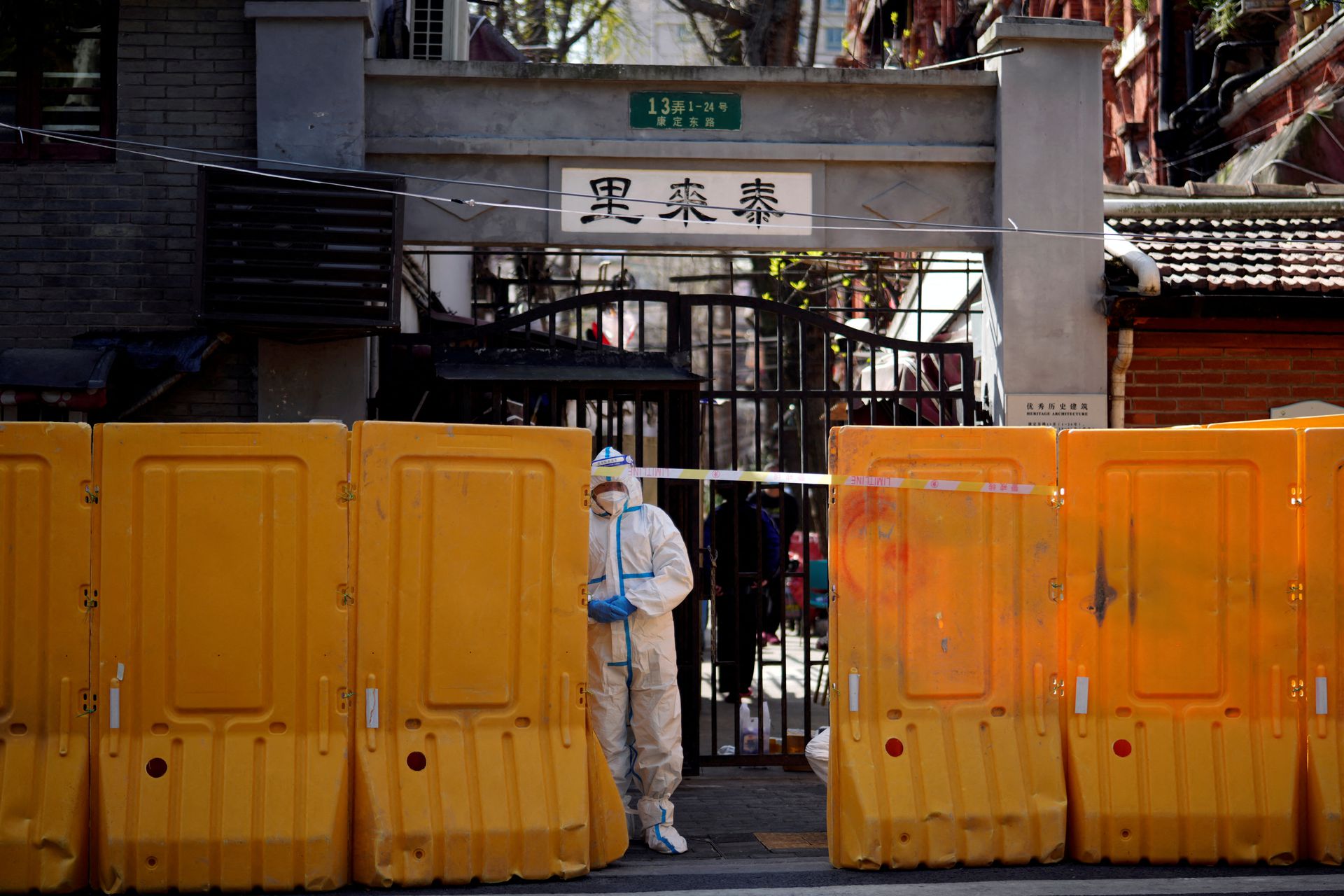 A worker in a protective suit stands behind barriers sealing off a residential area under lockdown, following the coronavirus disease outbreak in Shanghai, China, March 29, 2022.