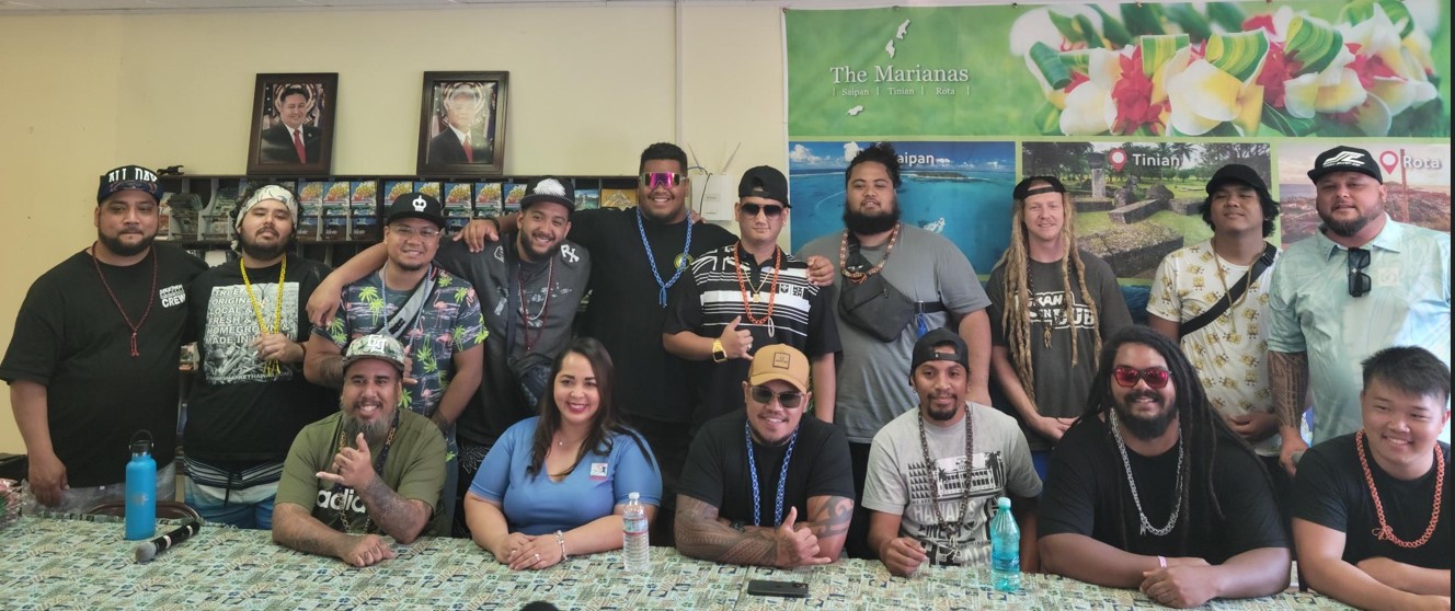 Marianas Visitors Authority Managing Director Priscilla Iakopo and Roil Soil Marketing owner and concert organizer Shayne Villanueva pose for a photo with the Hawaii reggae artists who will perform Friday evening at Garapan Fishing Base.