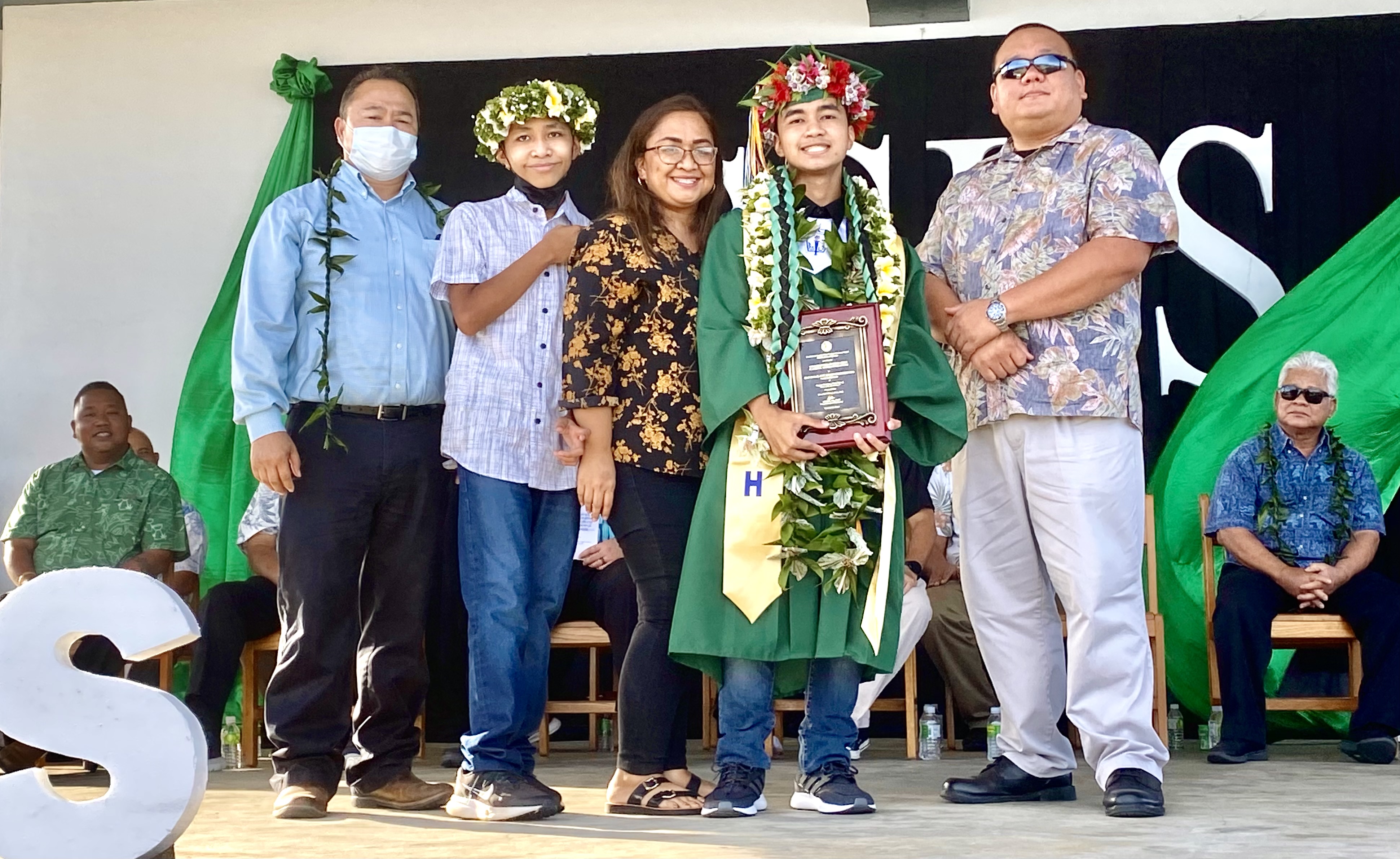 Salutatorian Juan Isaiah Jose Deleon Guerrero Ada receives the Commissioner of Education Award from Commissioner of Education Dr. Alfred B. Ada and Associate Commissioner Eric Magofna.  Also in photo are the salutatorian’s mother and sibling.