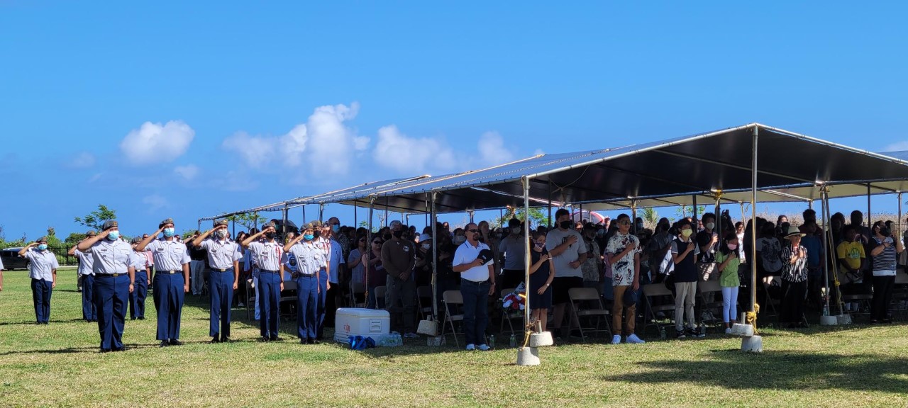 Community members stand during the singing of the national anthem.