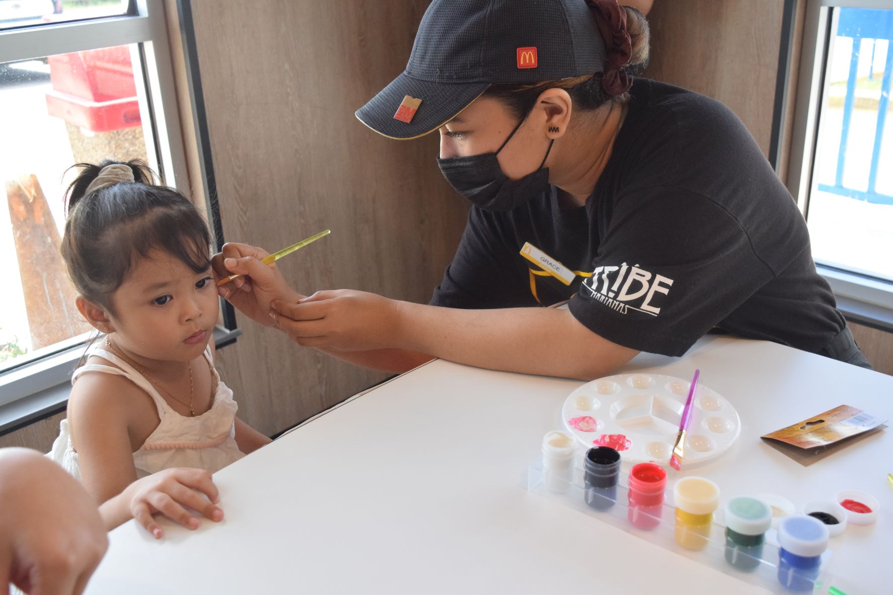 McDonald's young customer Jana Shanel Skye sits still as service crewmember Gracelun Babauta paints stars on her face.